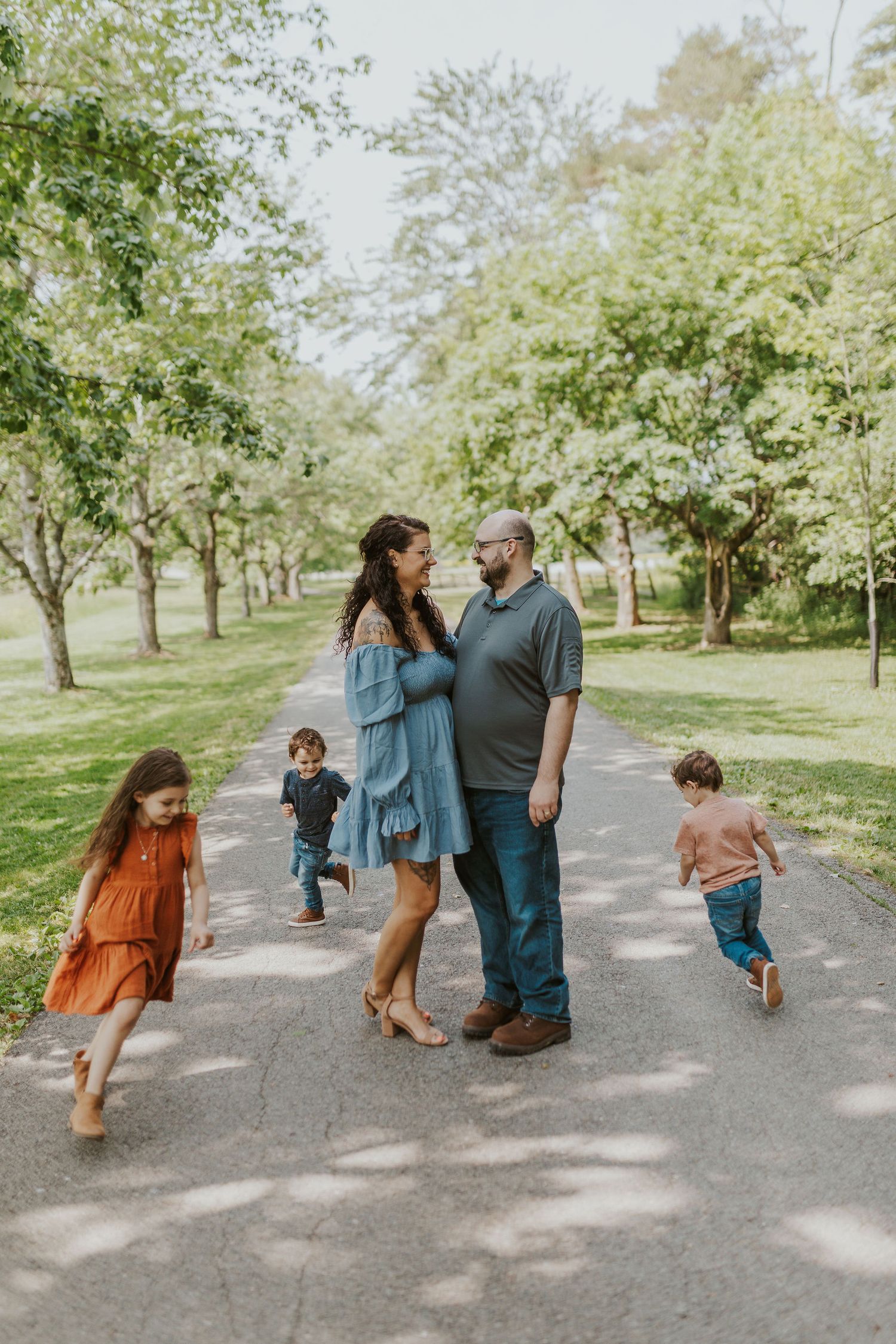 A family enjoying a casual stroll together on a tree-lined path on a sunny day.