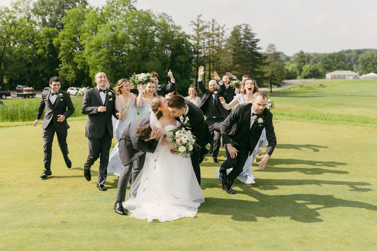 Wedding party members run and celebrate joyfully across a golf course green.