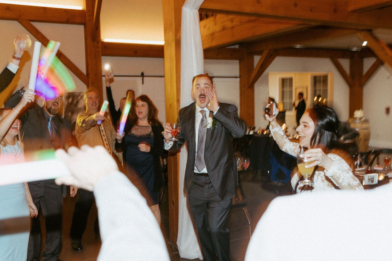 Wedding celebration in a rustic wooden beam venue with guests dancing under festive lighting.
