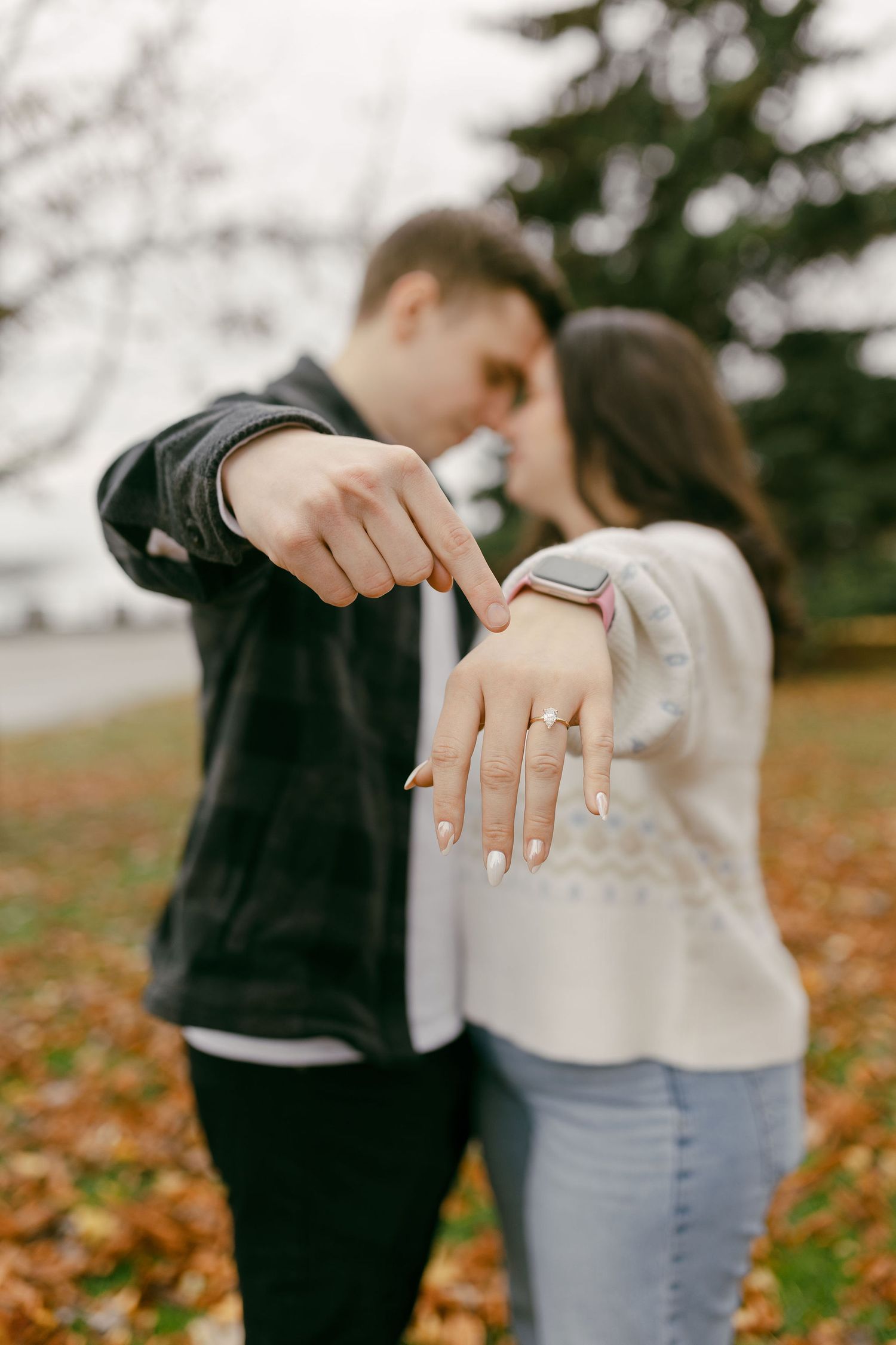 Couple showing off engagement ring outdoors in autumn park, woman wearing gold diamond ring and smartwatch.