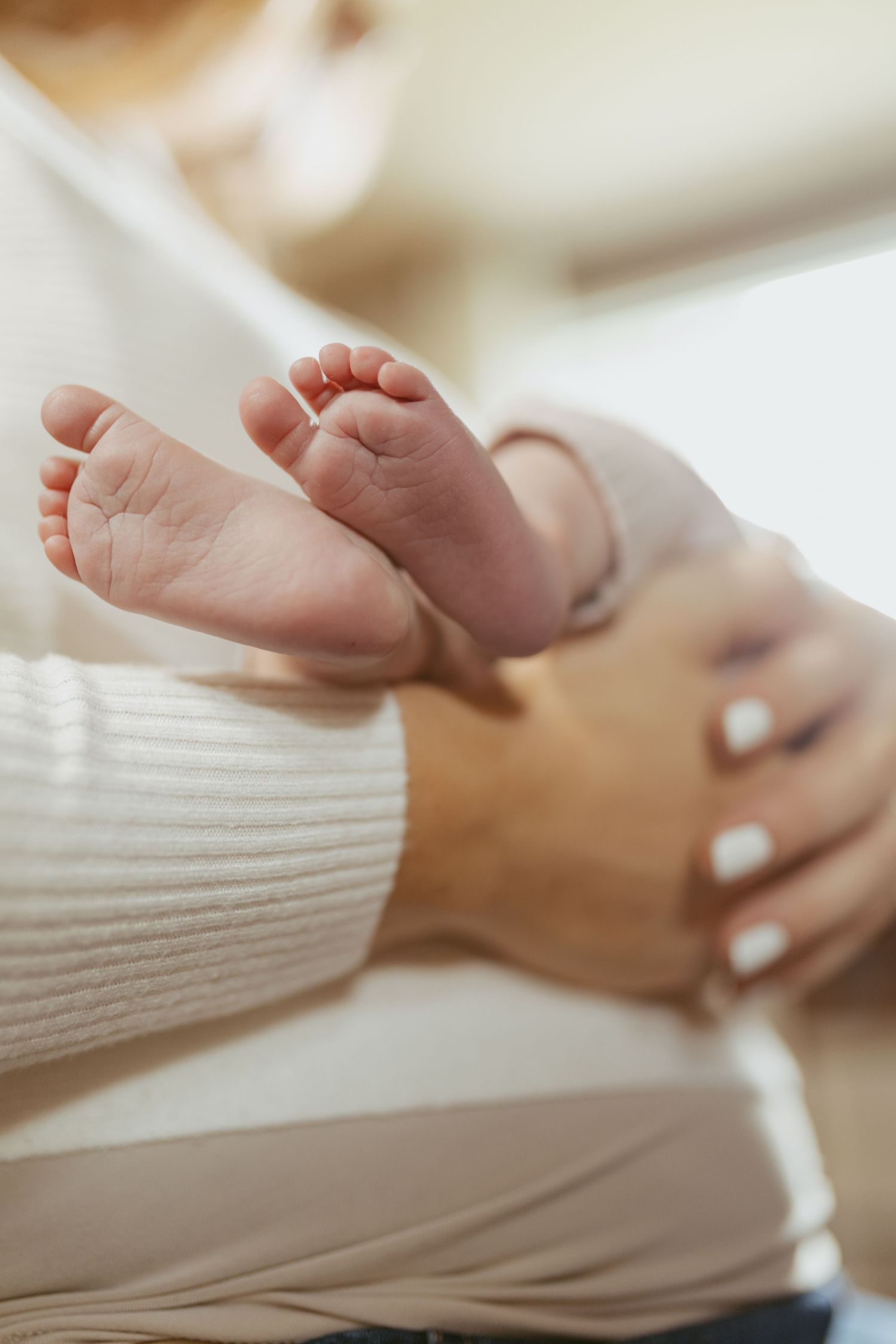 Close-up of tiny newborn baby feet resting gently on a mother's arm in a warm, soft-lit setting.