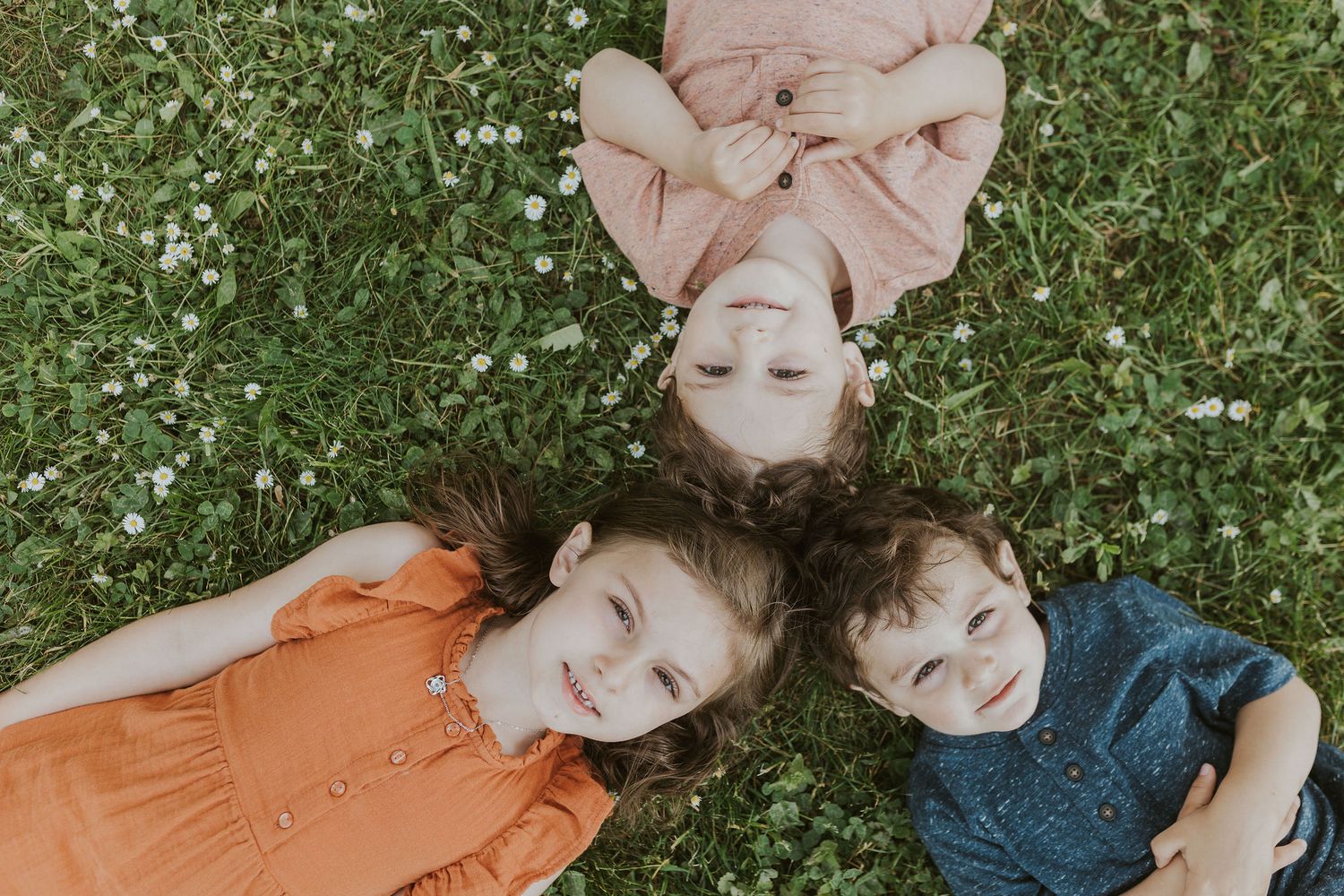 Children laying in green grass during a playful outdoor photo session.