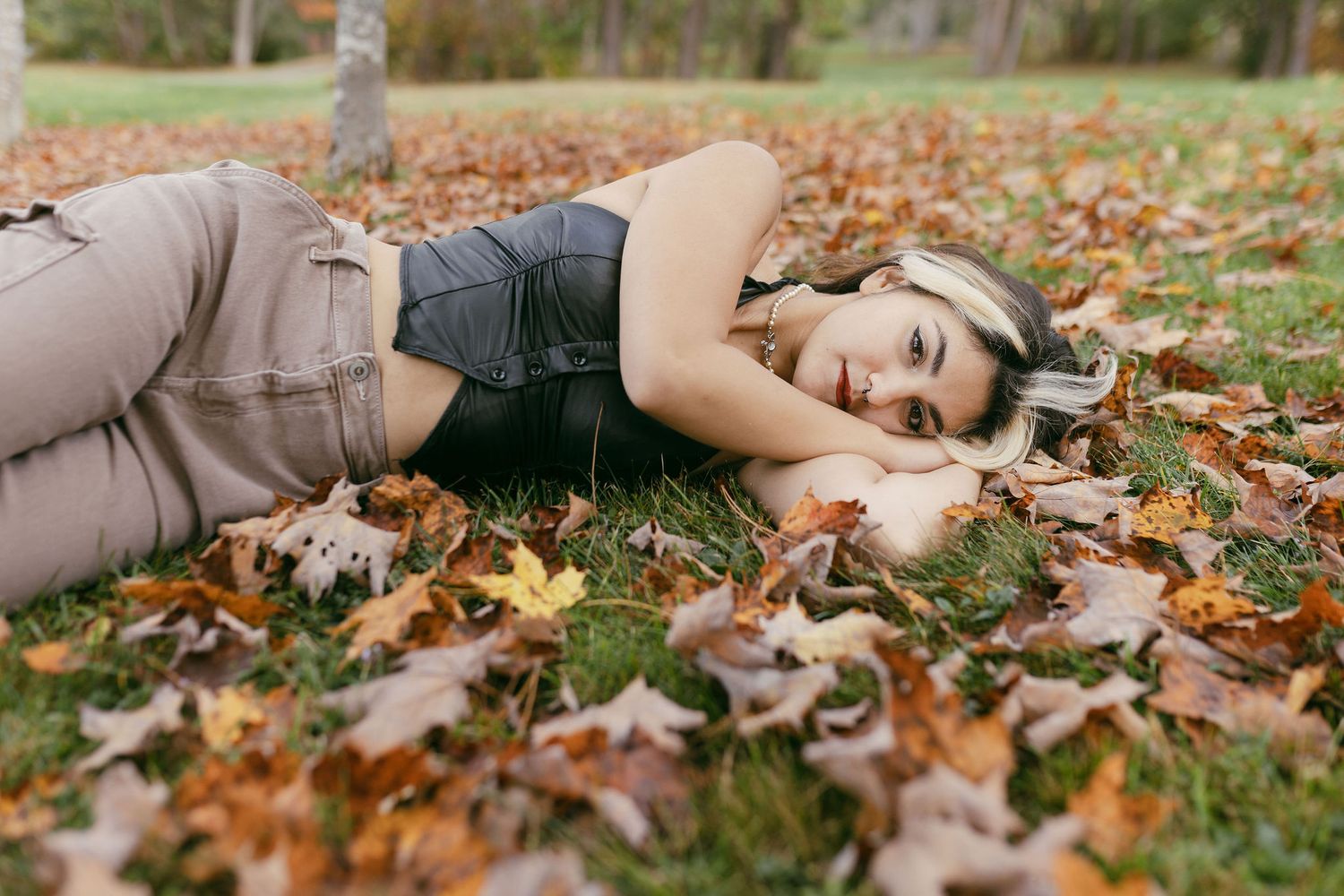 Lifestyle photography with subject lying among scattered autumn leaves on grass.