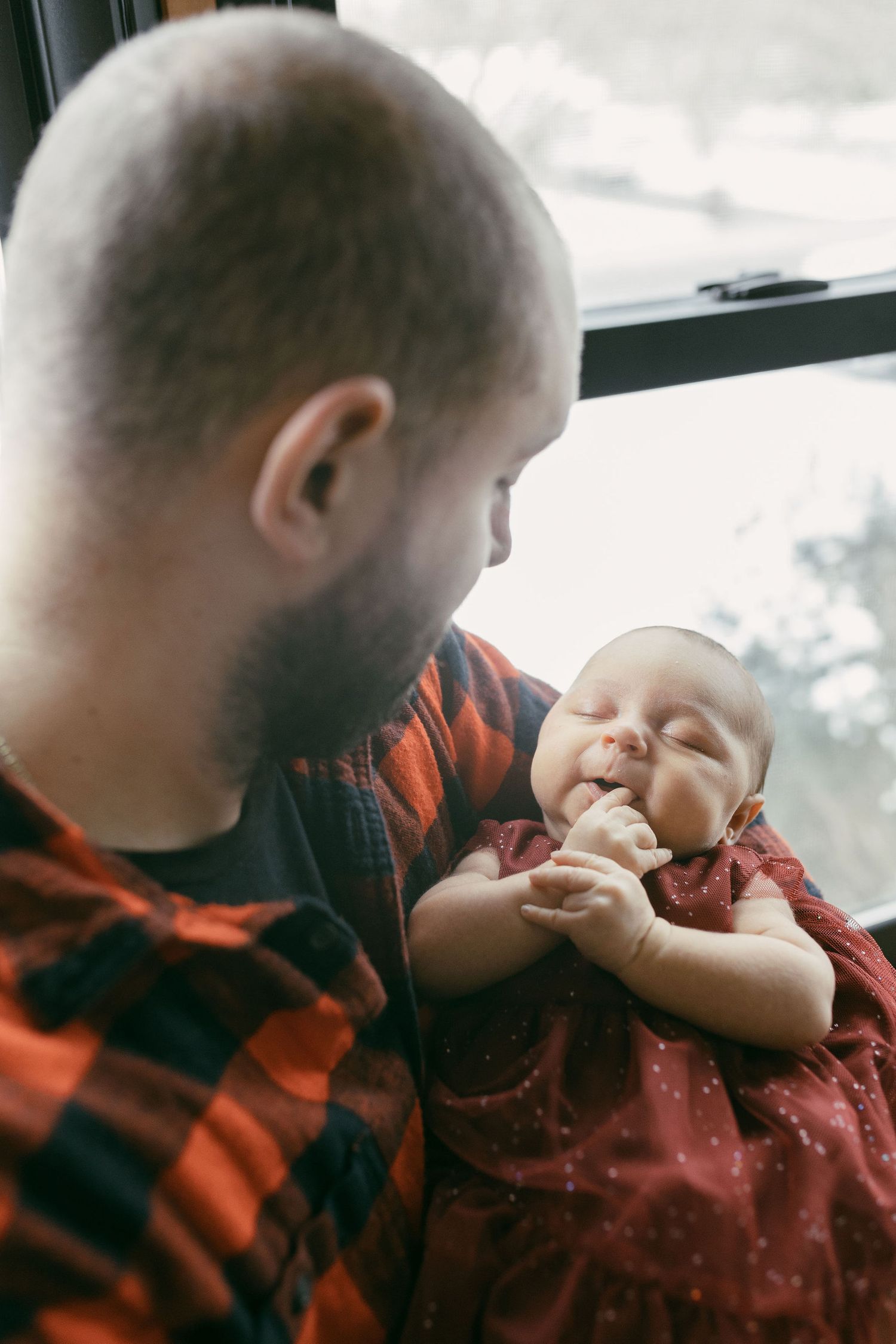 Person in red buffalo plaid shirt playing with baby in natural window light.