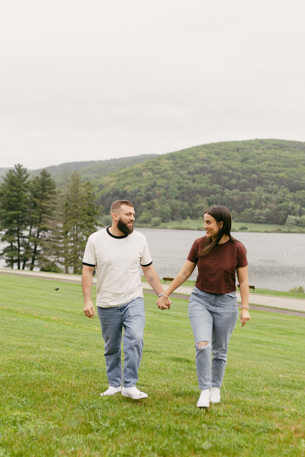 Couple walking hand in hand across green hillside with lake view.