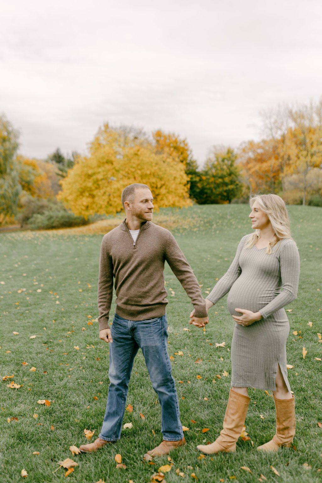 Couple holding hands during autumn maternity photoshoot in grassy field.