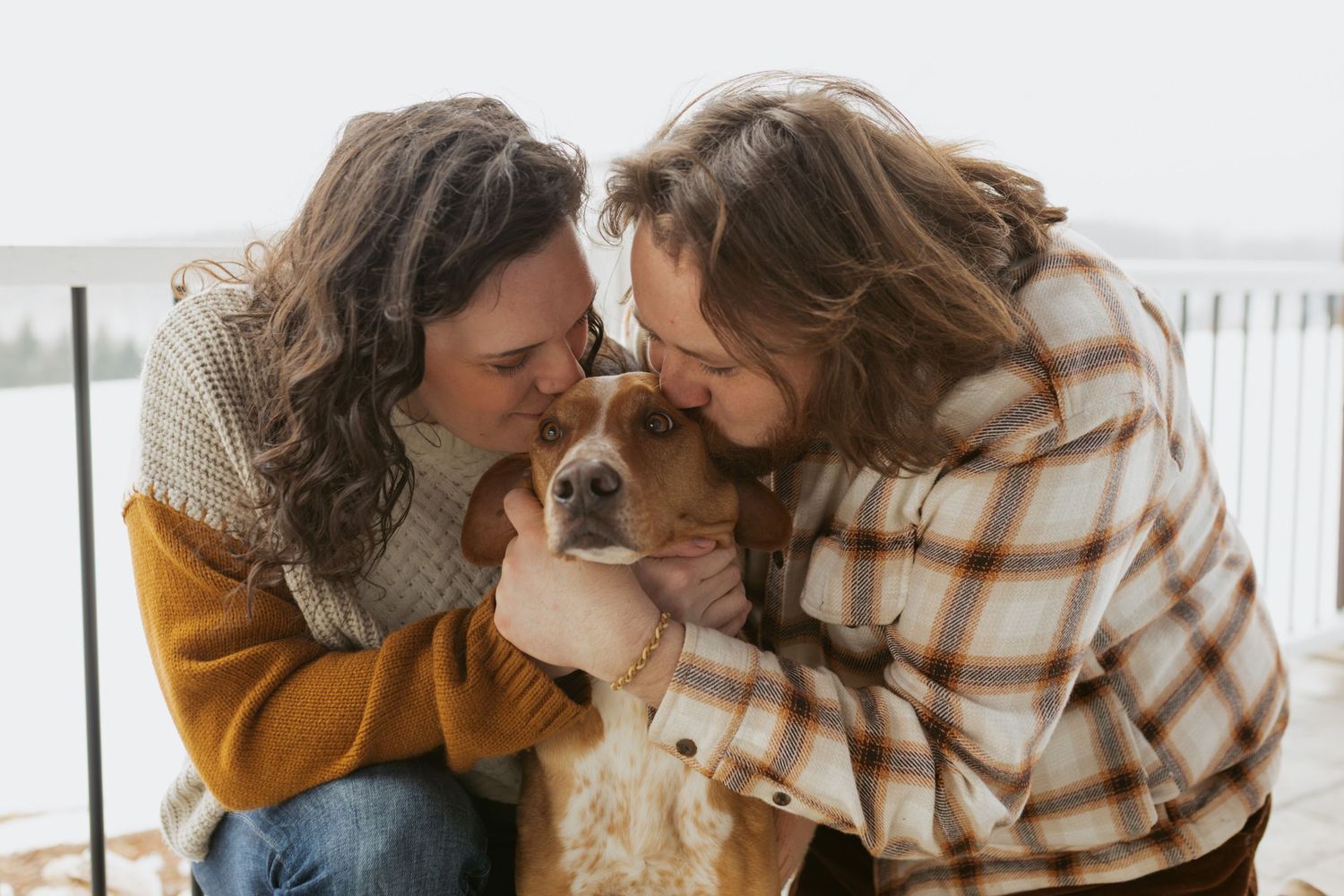 Two women kissing a golden dog outdoors in winter, sharing a joyful moment with their pet.