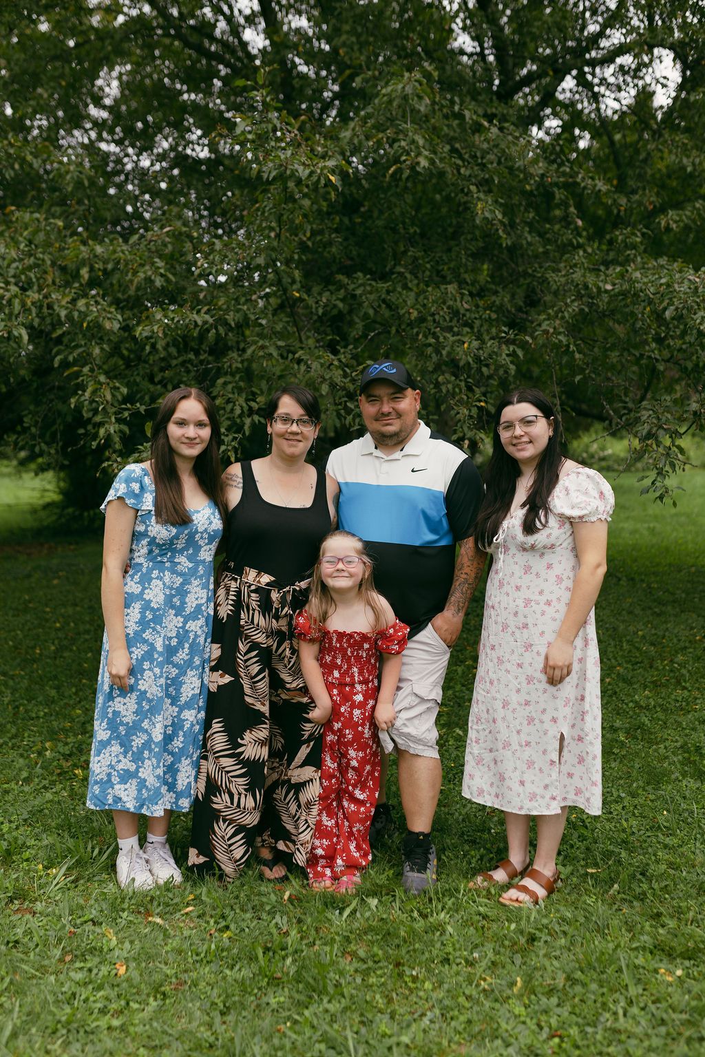 A group poses together on grass wearing coordinated floral and patterned outfits.
