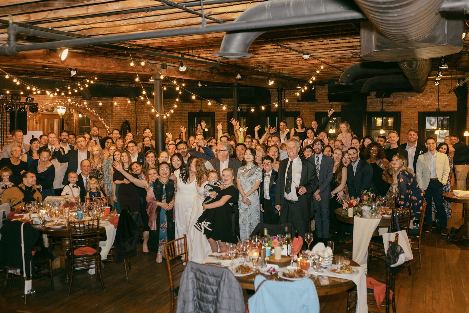 A warm-toned reception venue filled with guests and twinkling lights creating a festive atmosphere.