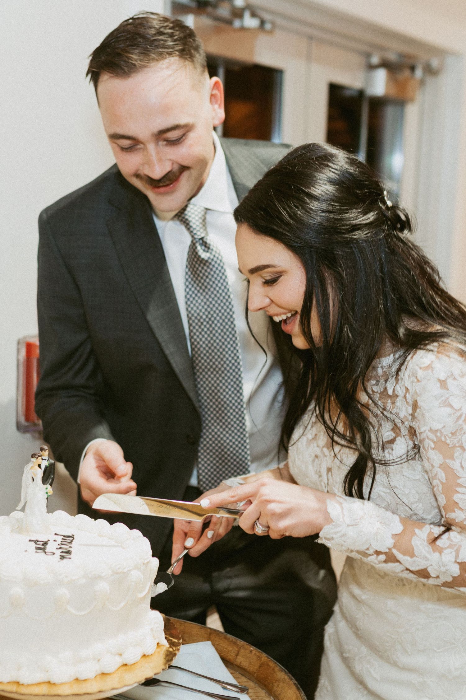 Newlyweds share a joyful moment while cutting their white wedding cake together.