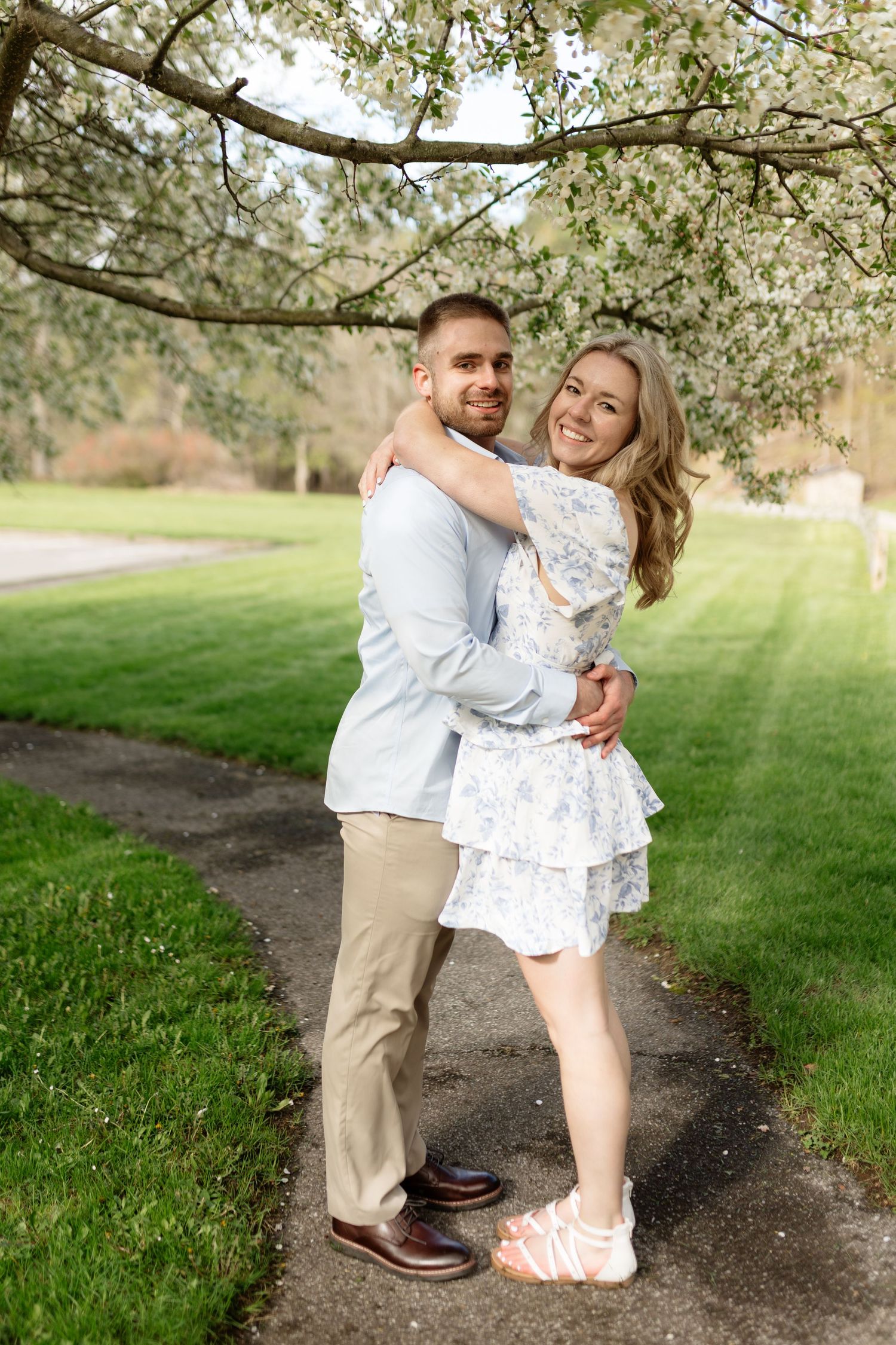 Couple embracing and smiling under blooming spring tree on garden path.