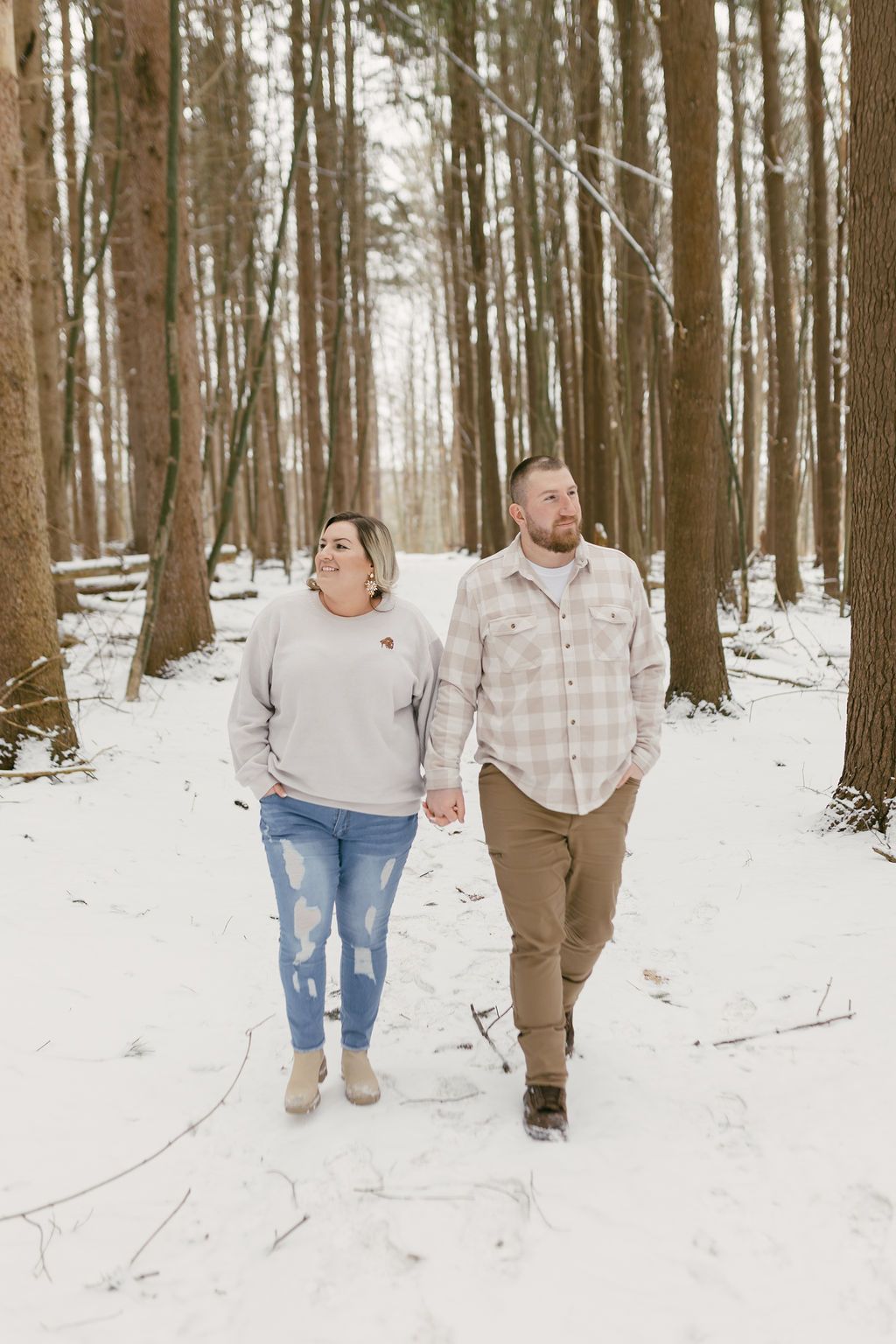 Couple walking through snowy forest path holding hands in winter.