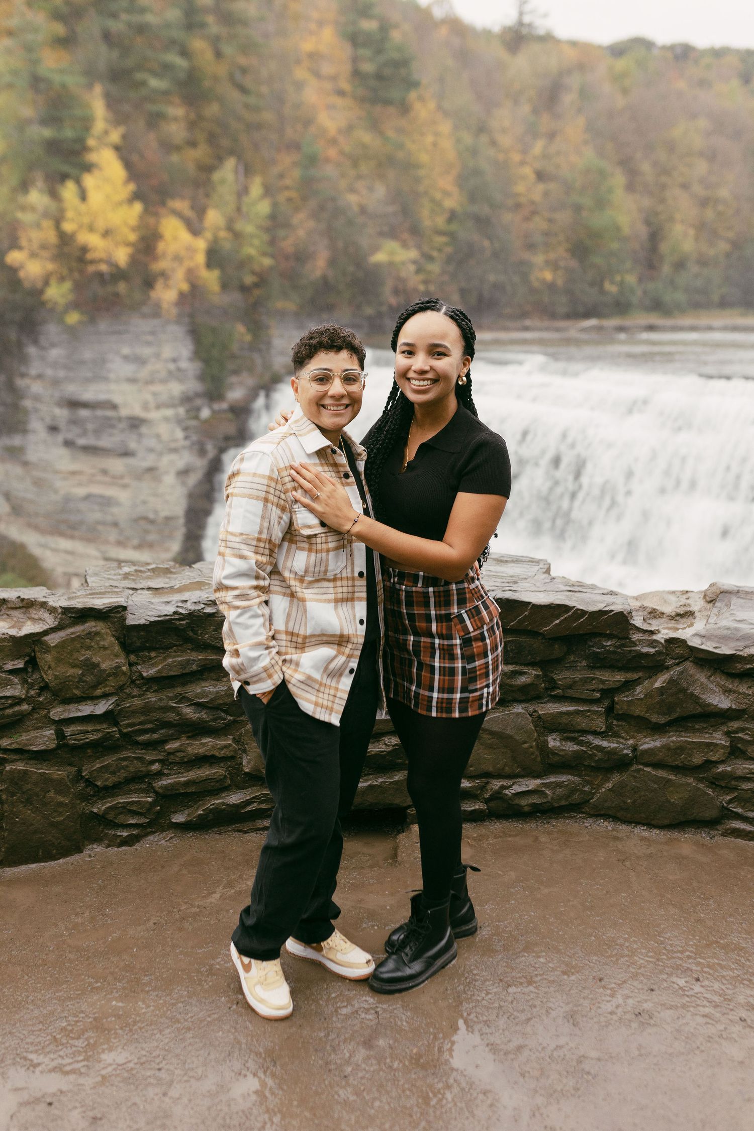 Couple sharing intimate moments by a scenic waterfall on rocky terrain.