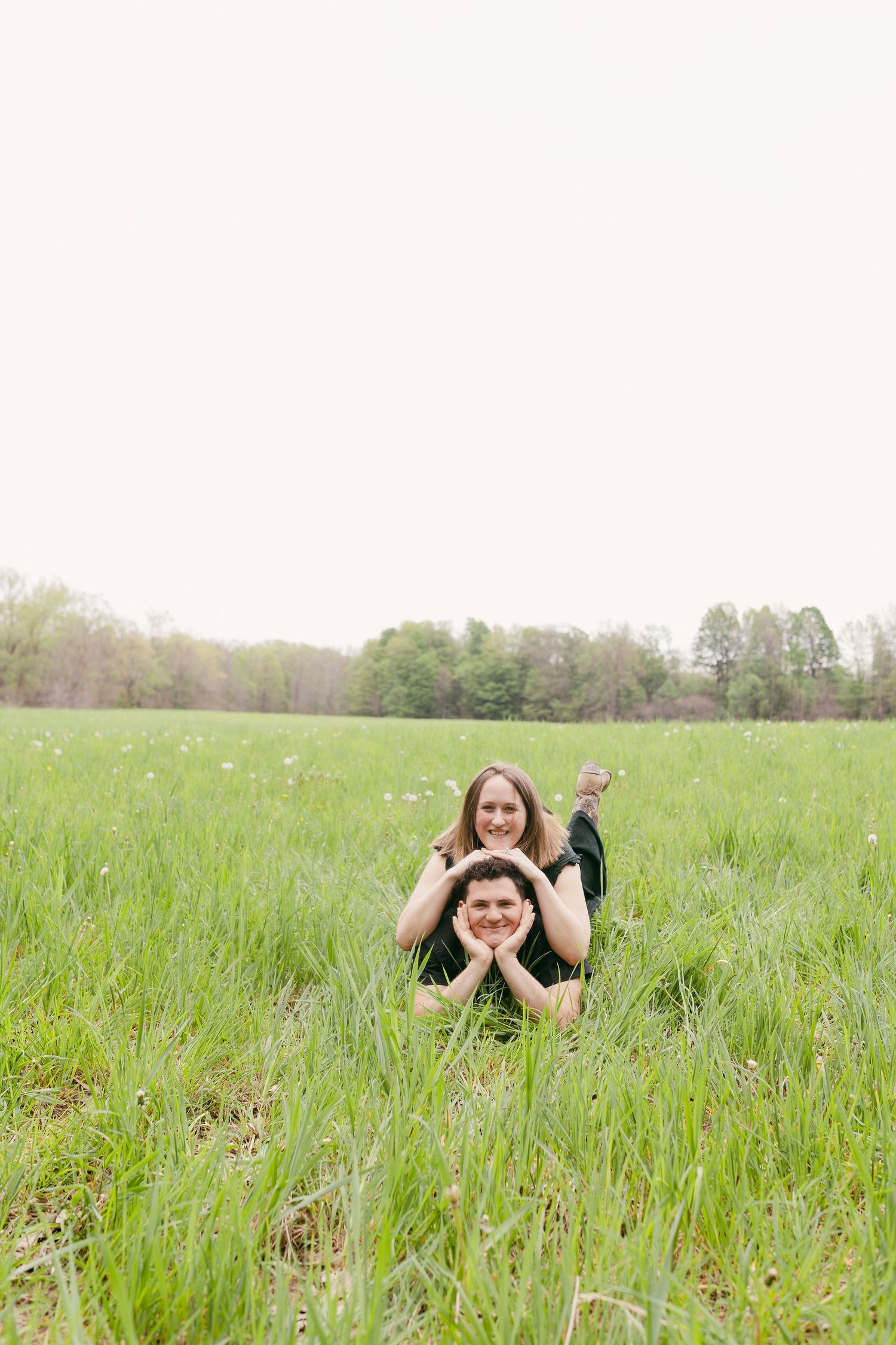 A person lies playfully in a lush green meadow filled with wildflowers on a sunny day.