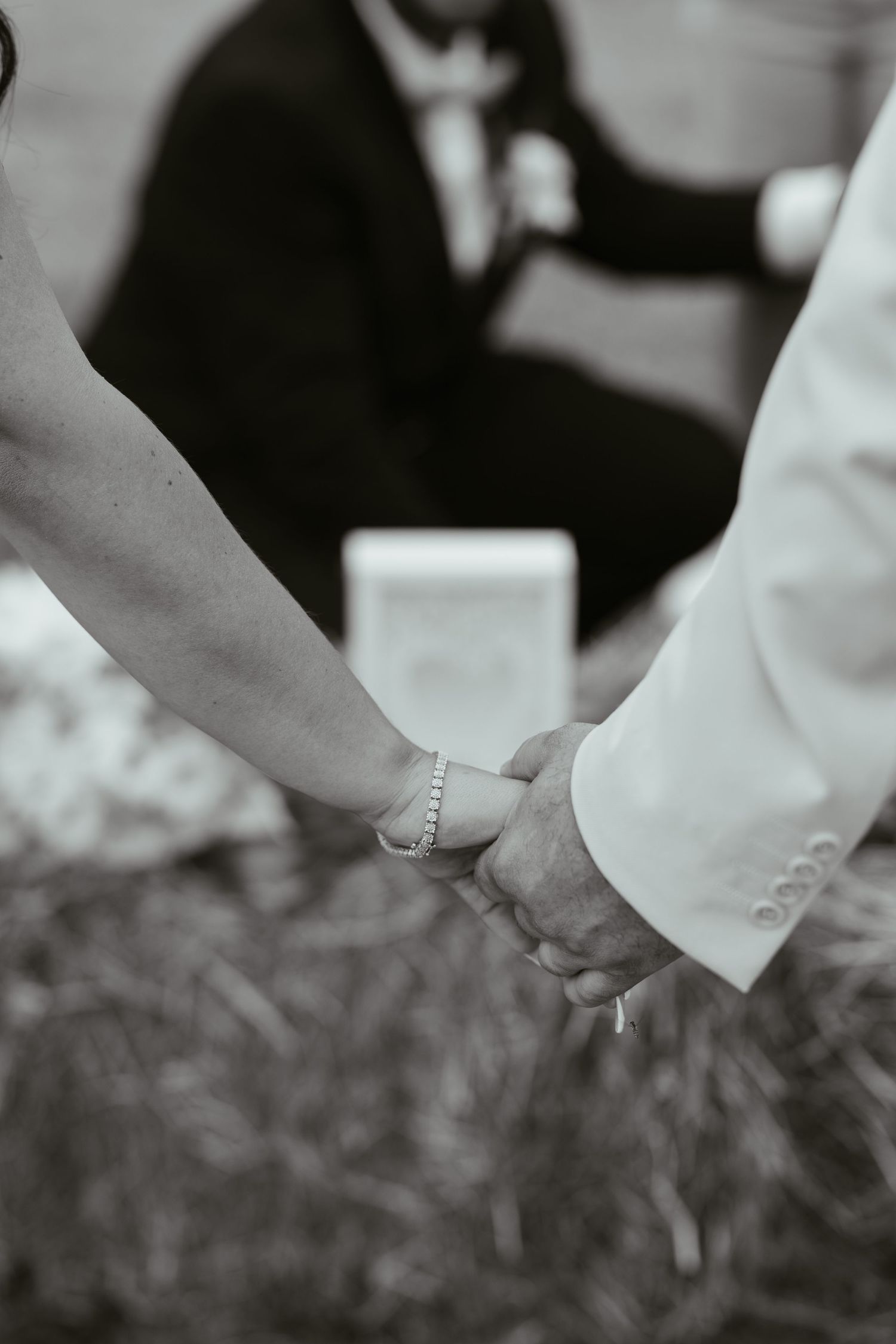 Black and white photo of a couple holding hands during a wedding ceremony, bride wearing a delicate bracelet.