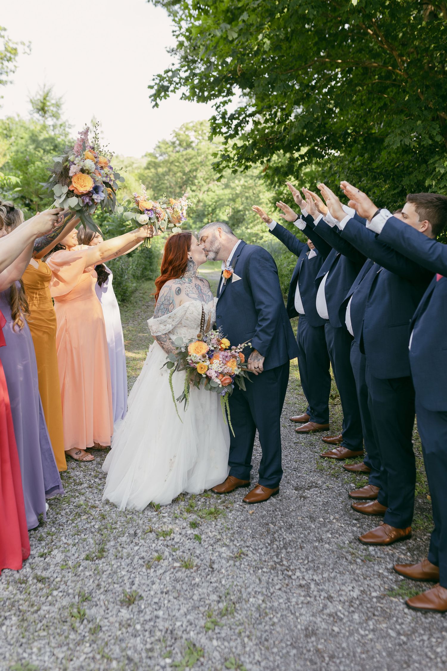 Wedding party in colorful dresses and suits lined up for fun photo on gravel path.