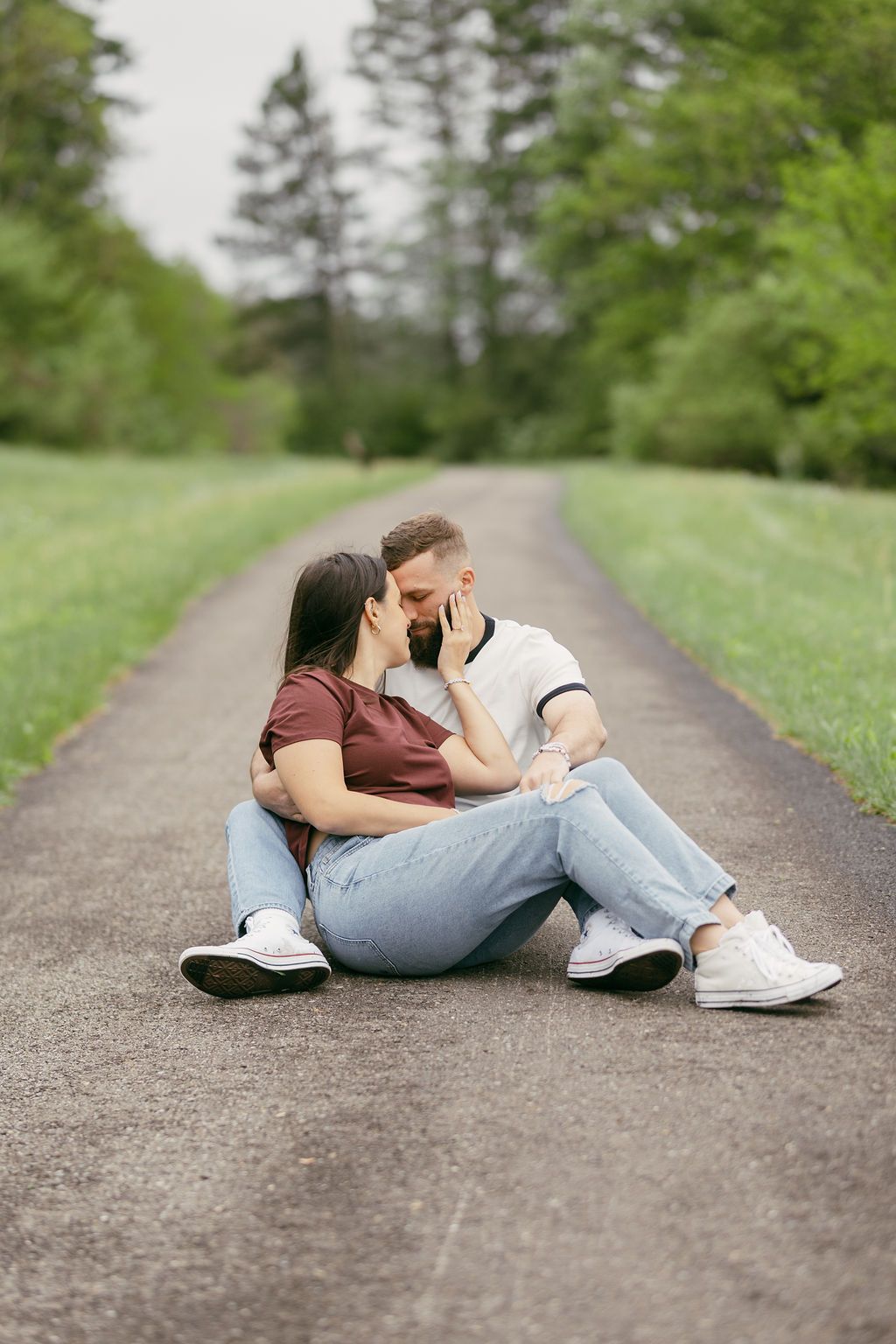 Couple lying together on a path surrounded by green scenery.