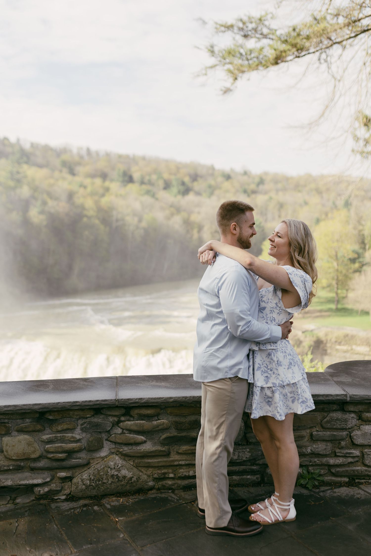 Romantic couple hugging on stone terrace overlooking scenic waterfall and forest.