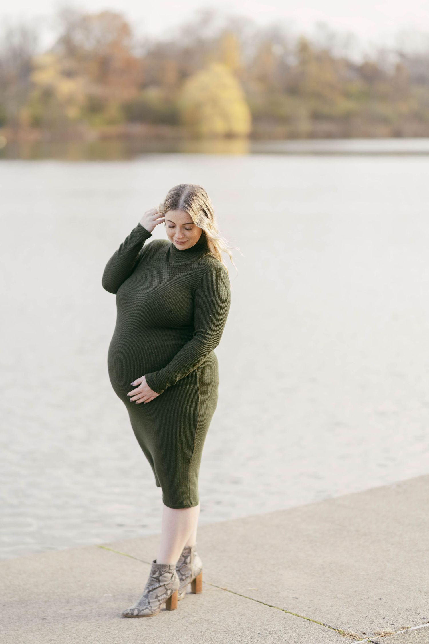 Maternity portrait of woman in dark dress posing by waterfront.