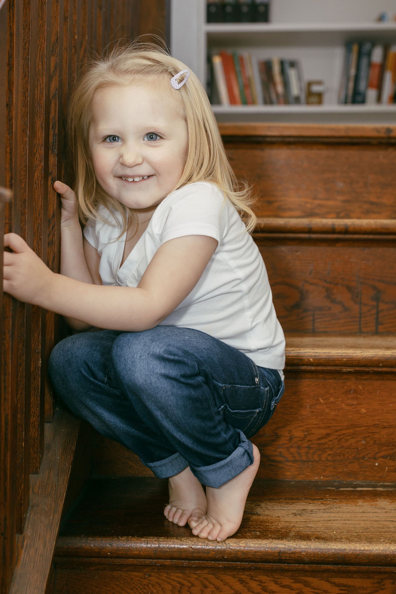 Small child sitting on wooden stairs indoors wearing casual clothes.