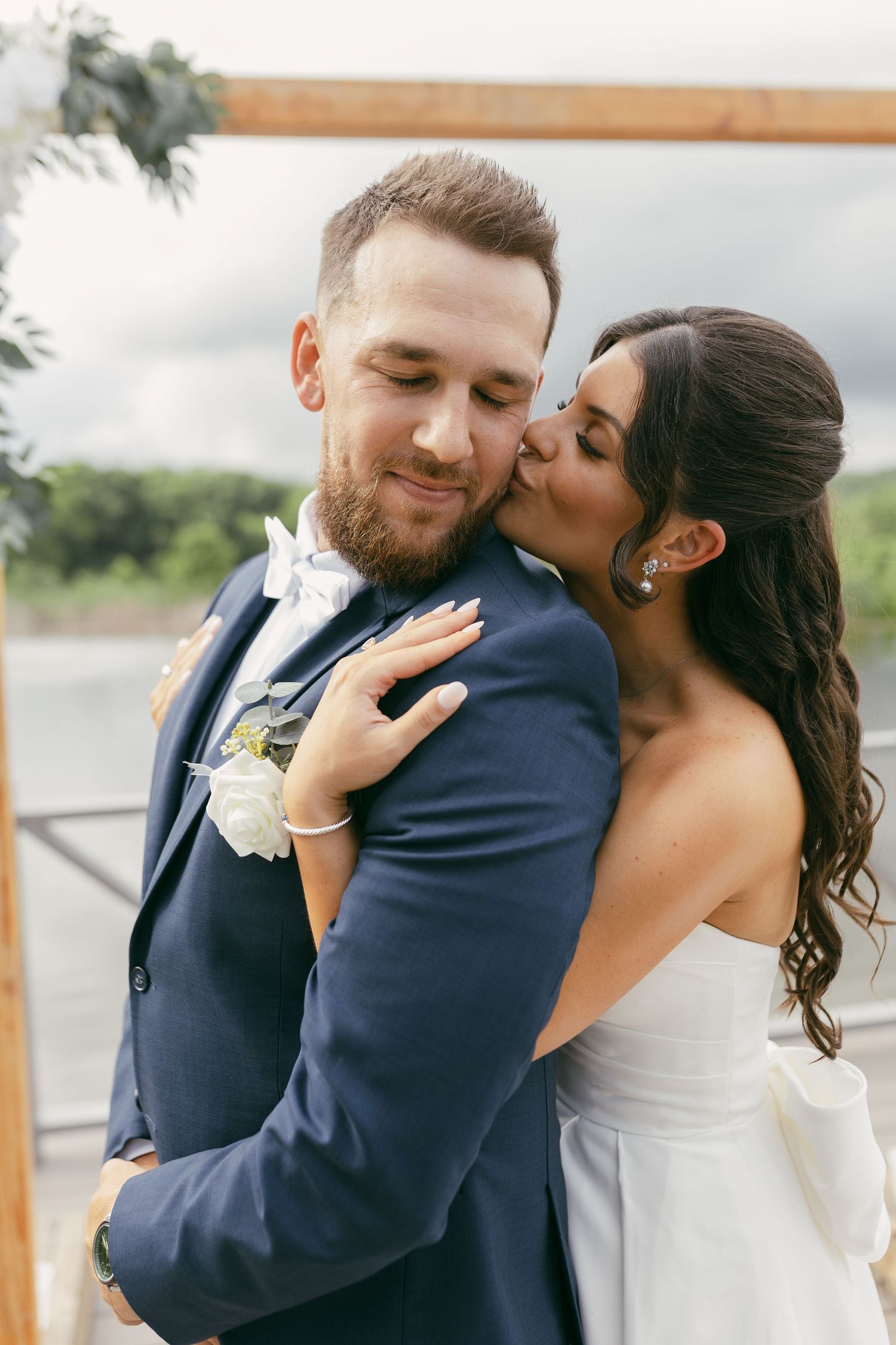 Romantic moment captured under wooden arbor by waterfront.