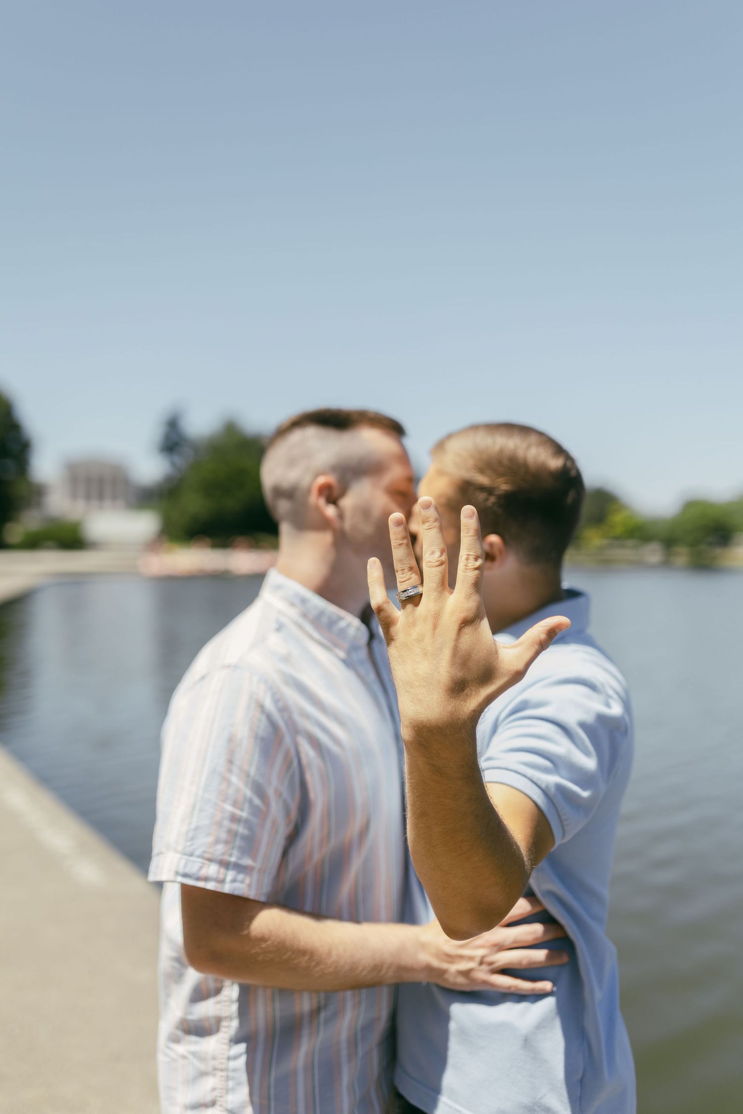 Two people embracing by a waterfront on a sunny day.