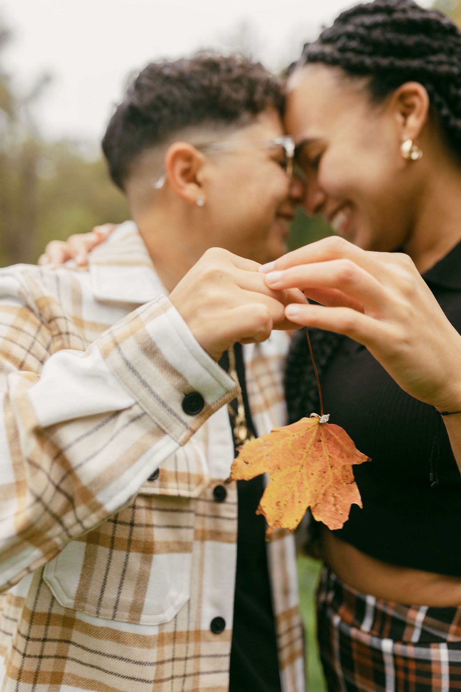 Hands holding an autumn maple leaf against a blurred natural background.