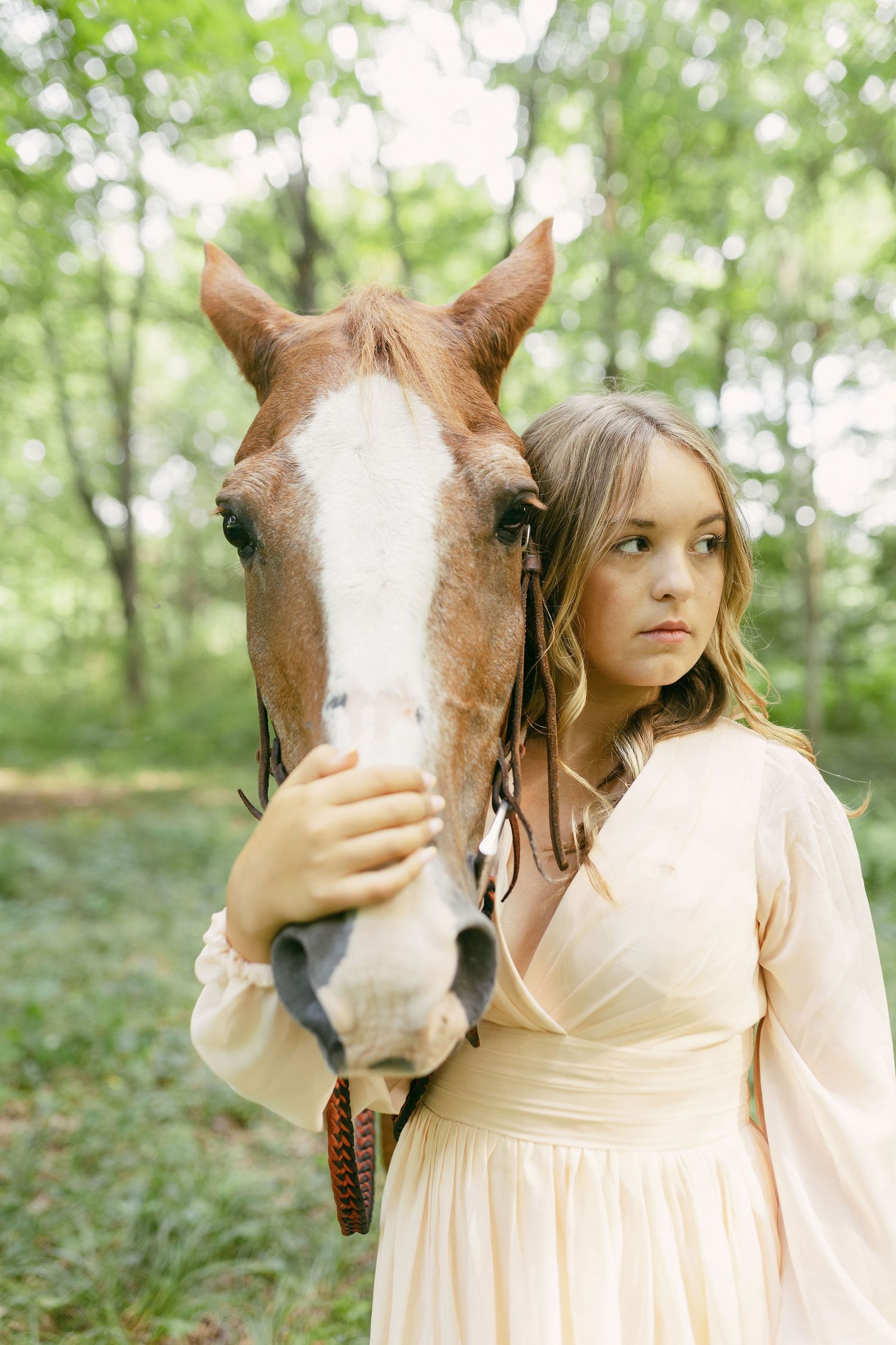 A brown and white horse with a white blaze stands close to someone in a cream-colored dress.
