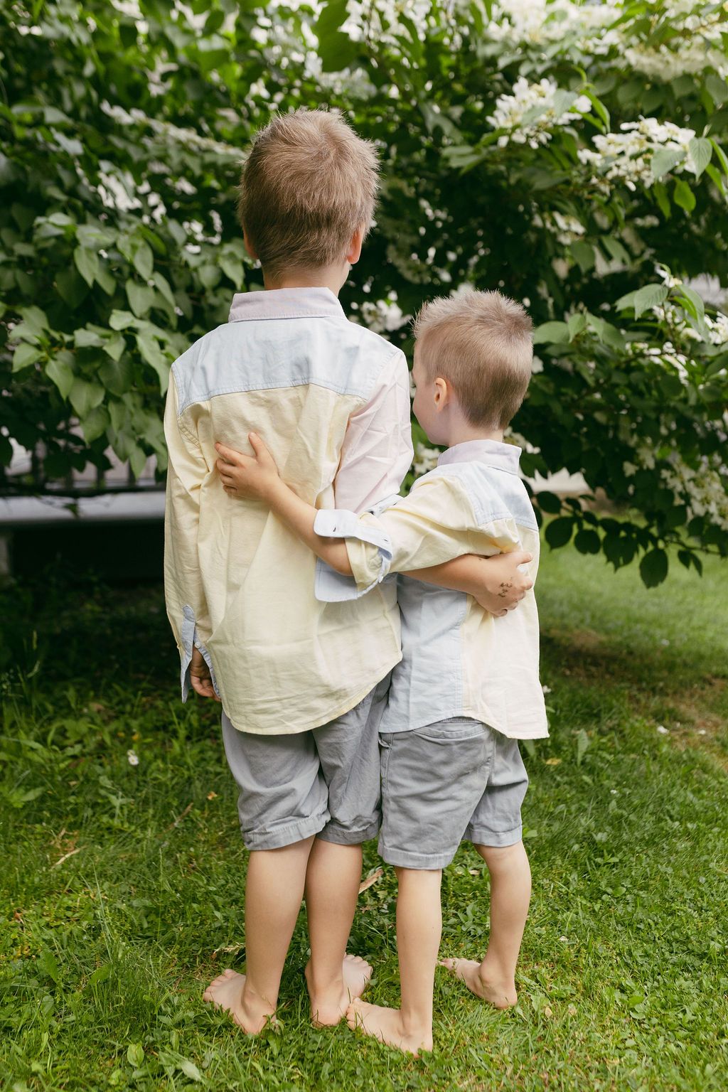 Three children in matching light colored outfits standing together with arms around each other.