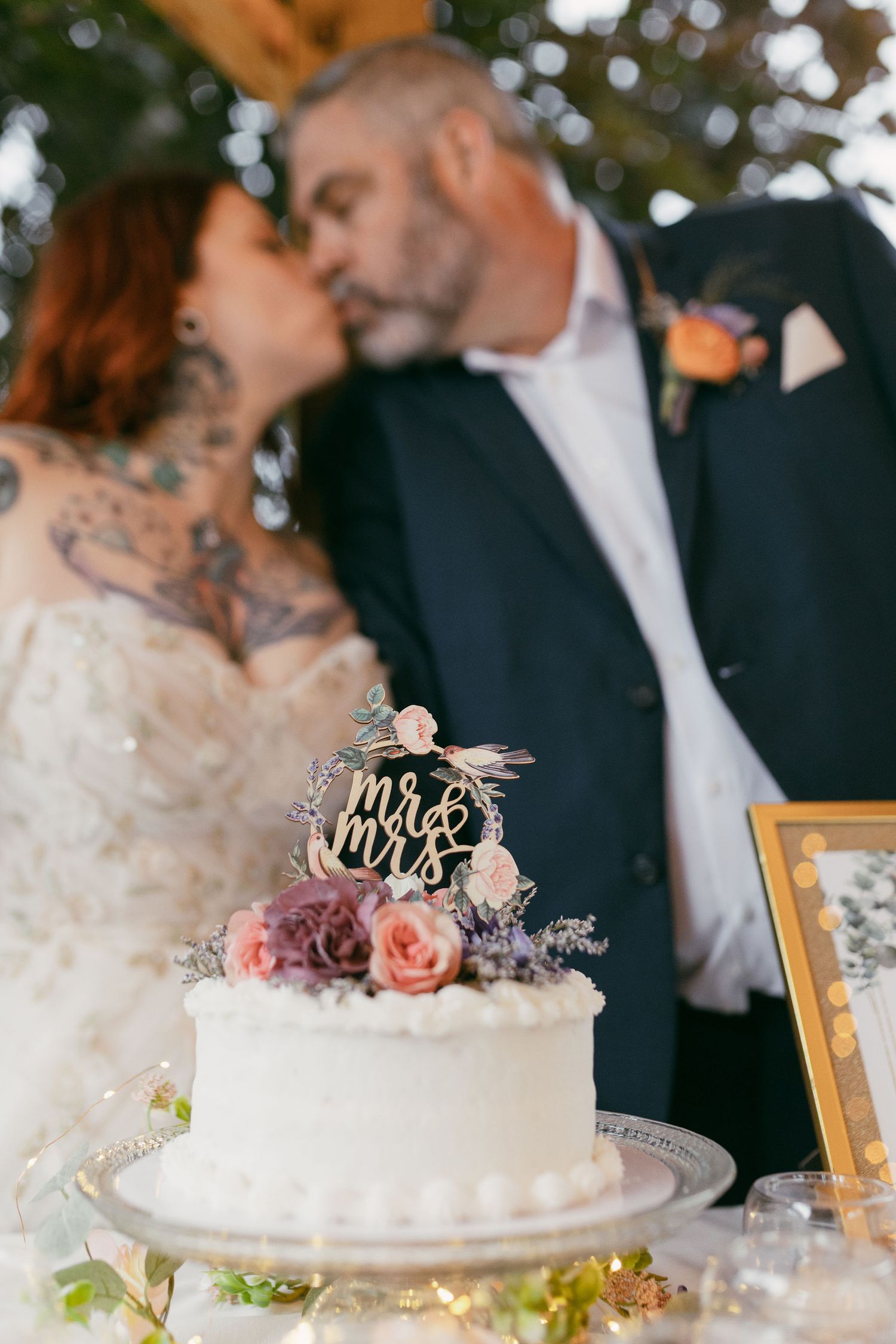 White wedding cake decorated with roses and 'Mr & Mrs' topper on display.