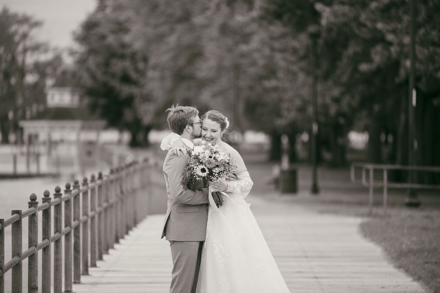 Wedding party poses in a line on a rustic wooden walkway with white fencing.