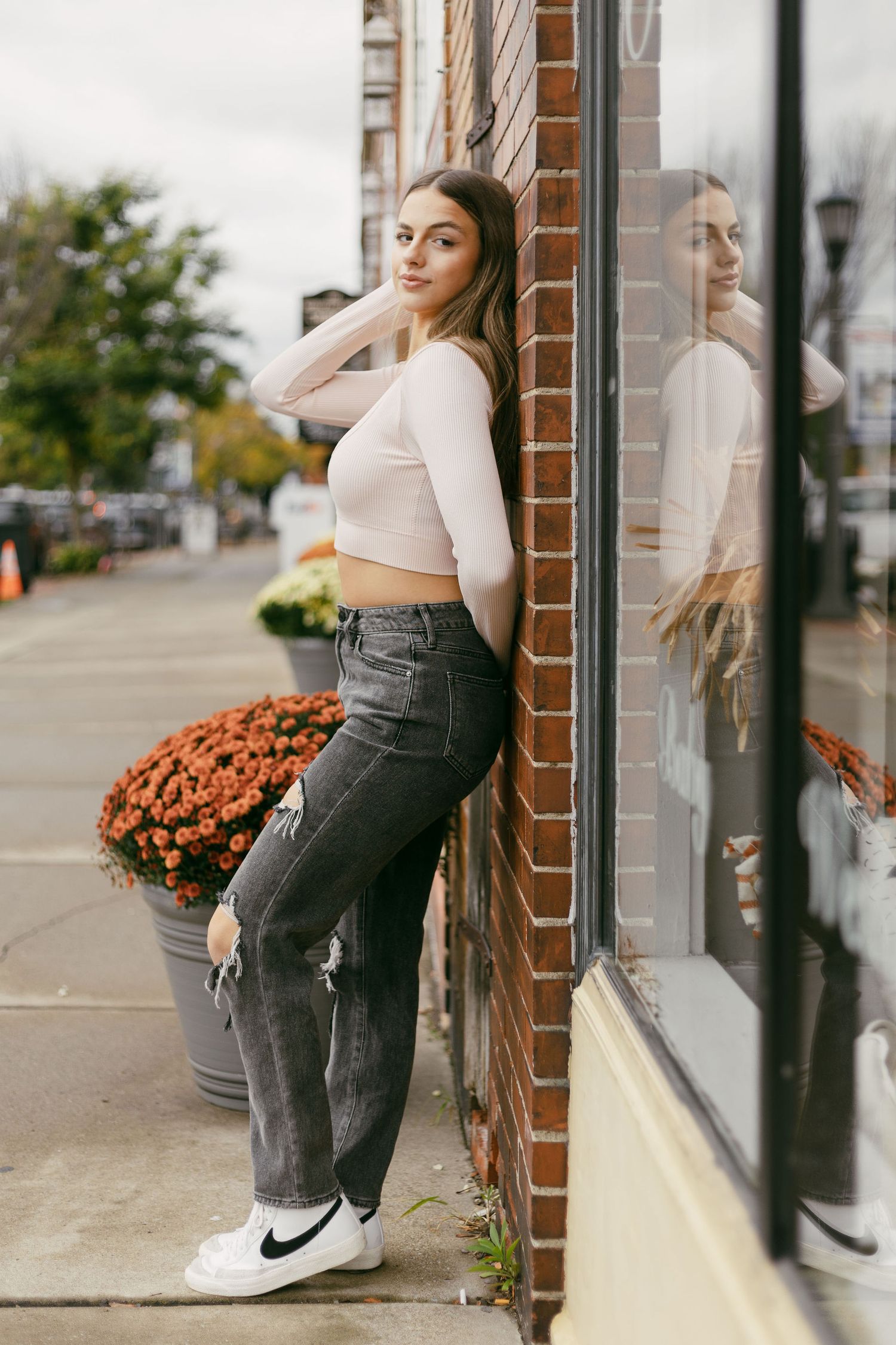 Someone in casual attire poses against a brick wall with autumn decorations nearby.