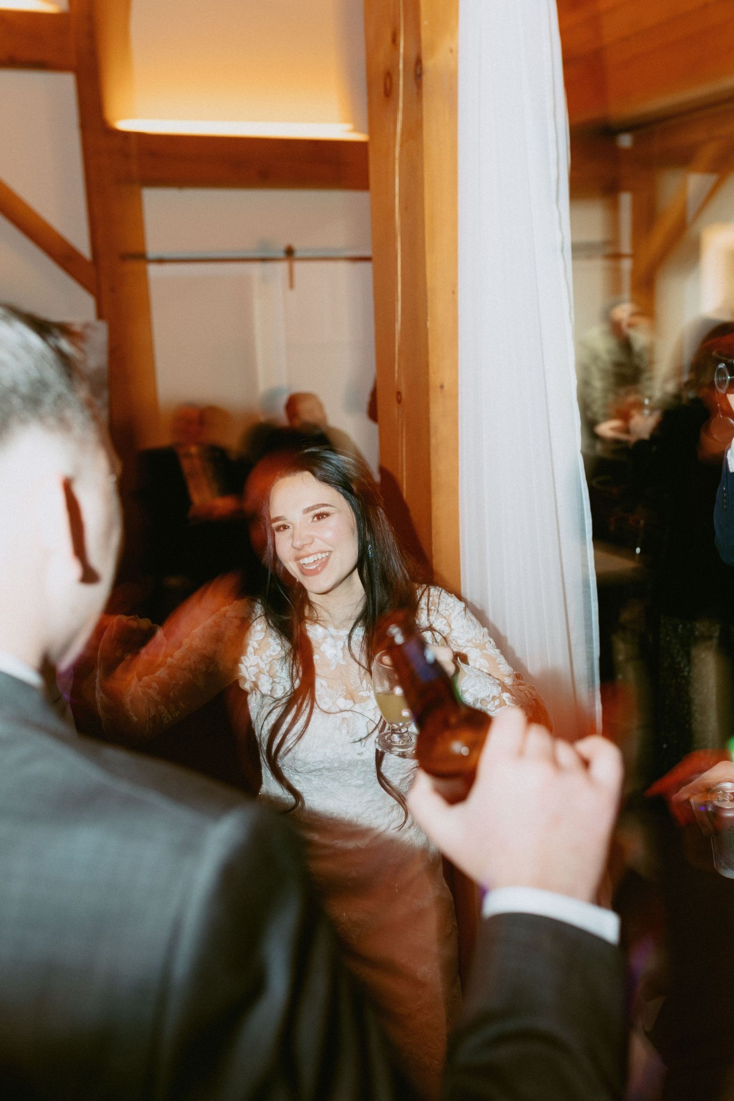 Candid moments captured during a wedding reception with guests dancing in a timber-framed venue.