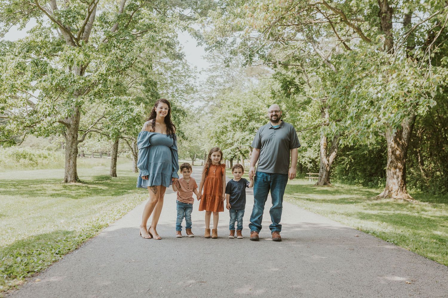 Family walking together on a tree-lined path during an outdoor photo session.