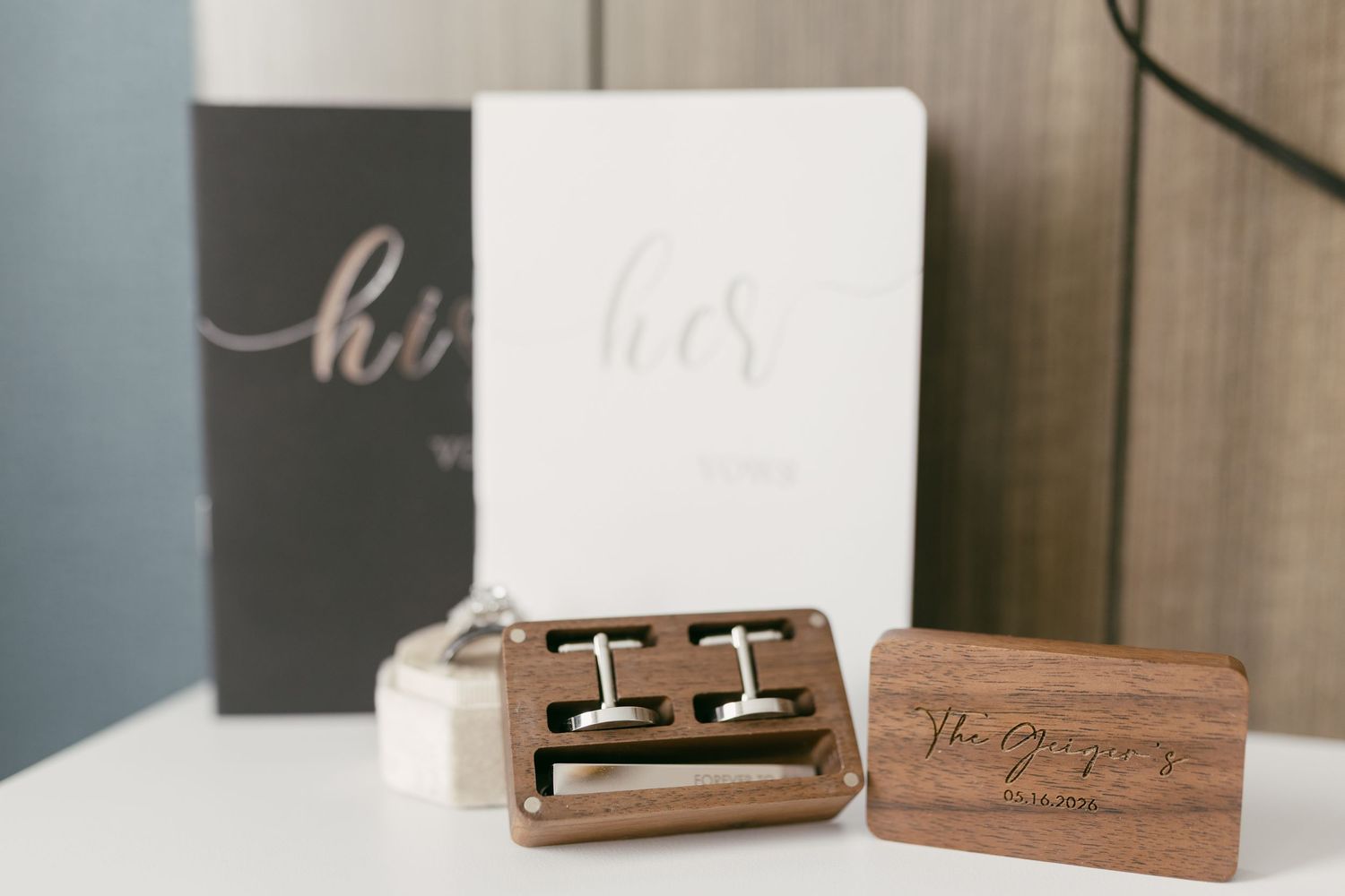 Personalized wooden cufflink box with engraving beside his and hers wedding vow books on white table.