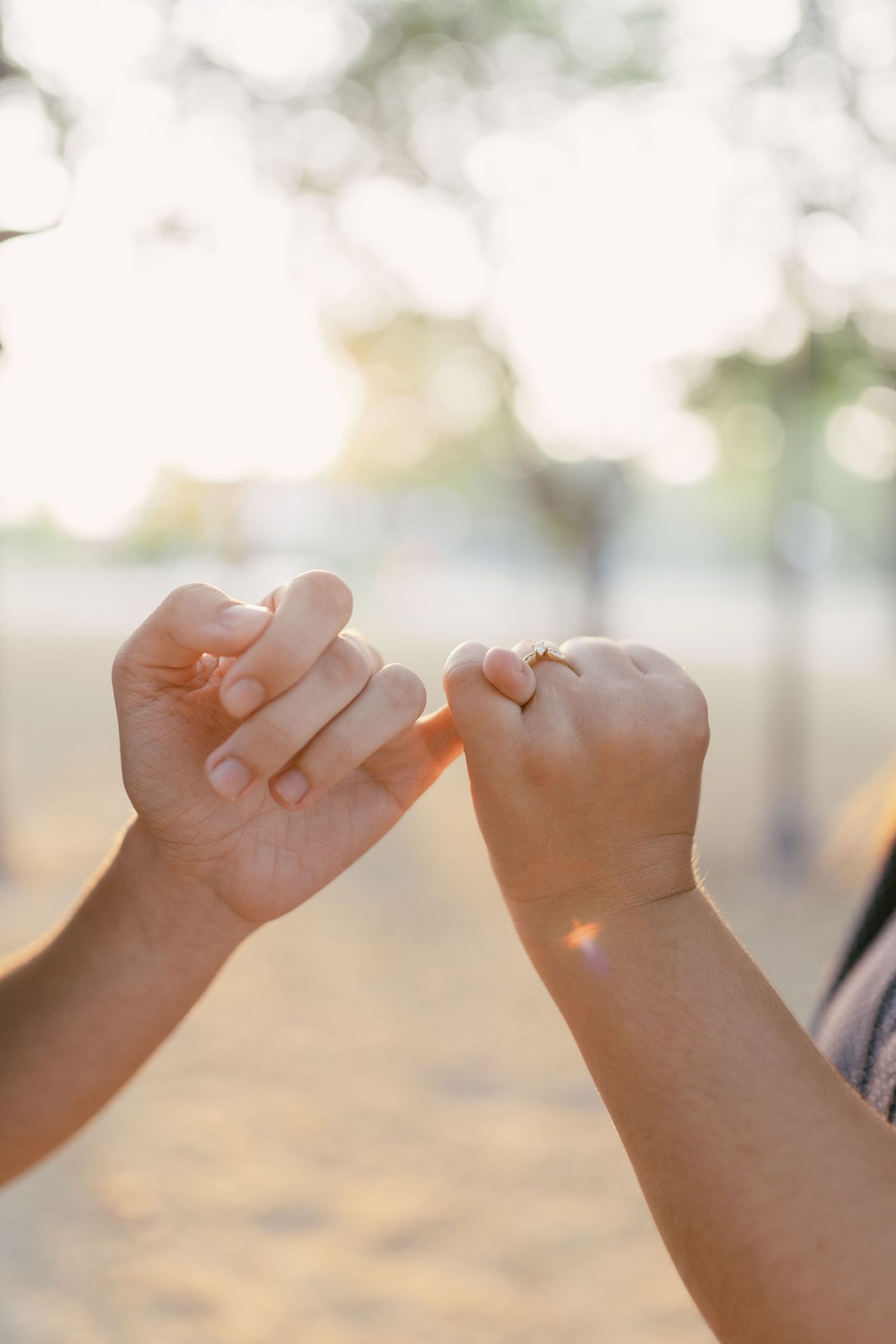 Two hands making a pinky promise gesture in warm golden sunlight with soft bokeh background.