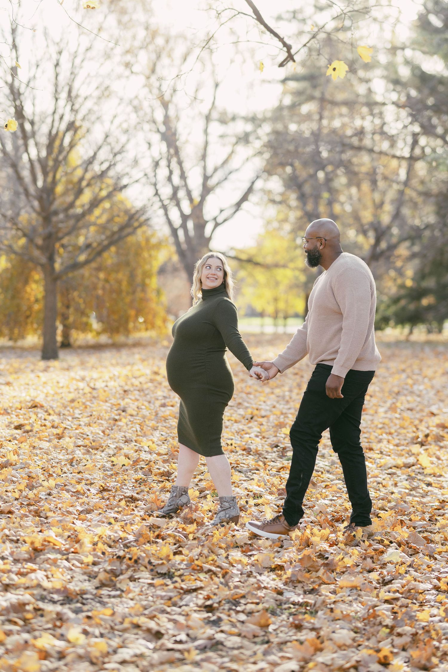 Autumn maternity photo of couple holding hands among fallen leaves.