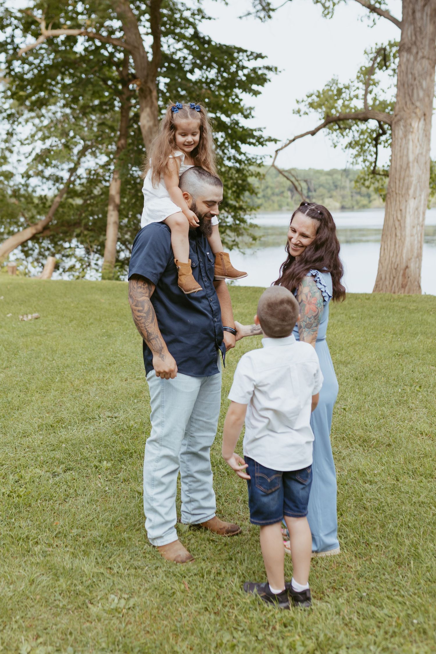 Happy family of four enjoying a sunny day outdoors near a lake, with dad giving daughter a piggyback ride.