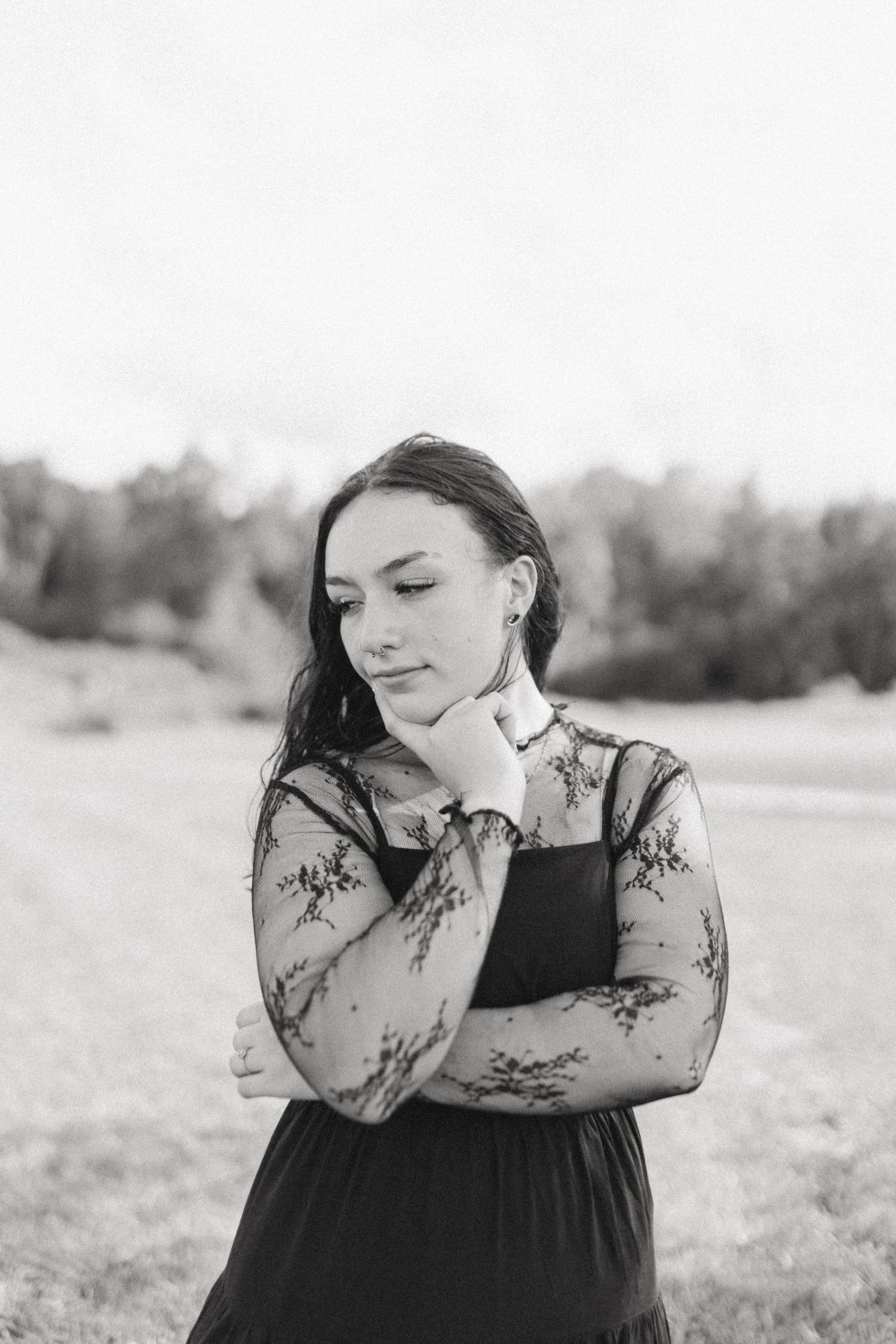 Black and white portrait of a young woman in floral lace dress posing thoughtfully outdoors in a field.