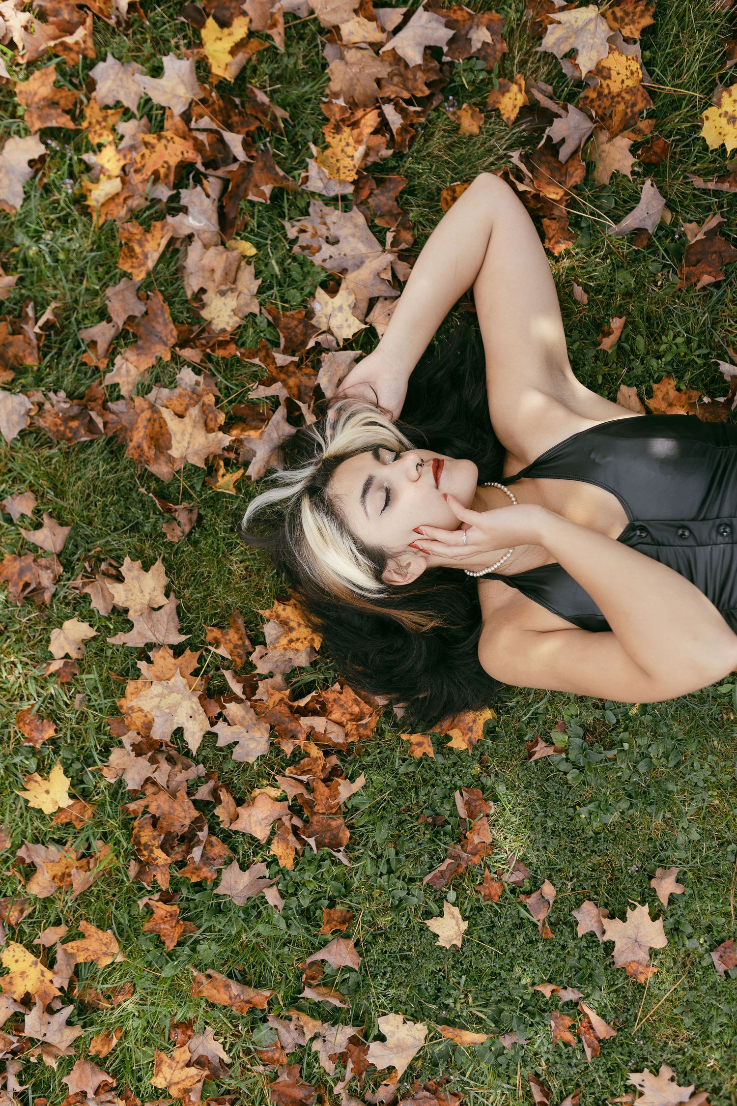 Artistic autumn portraits on grass surrounded by scattered fall leaves.