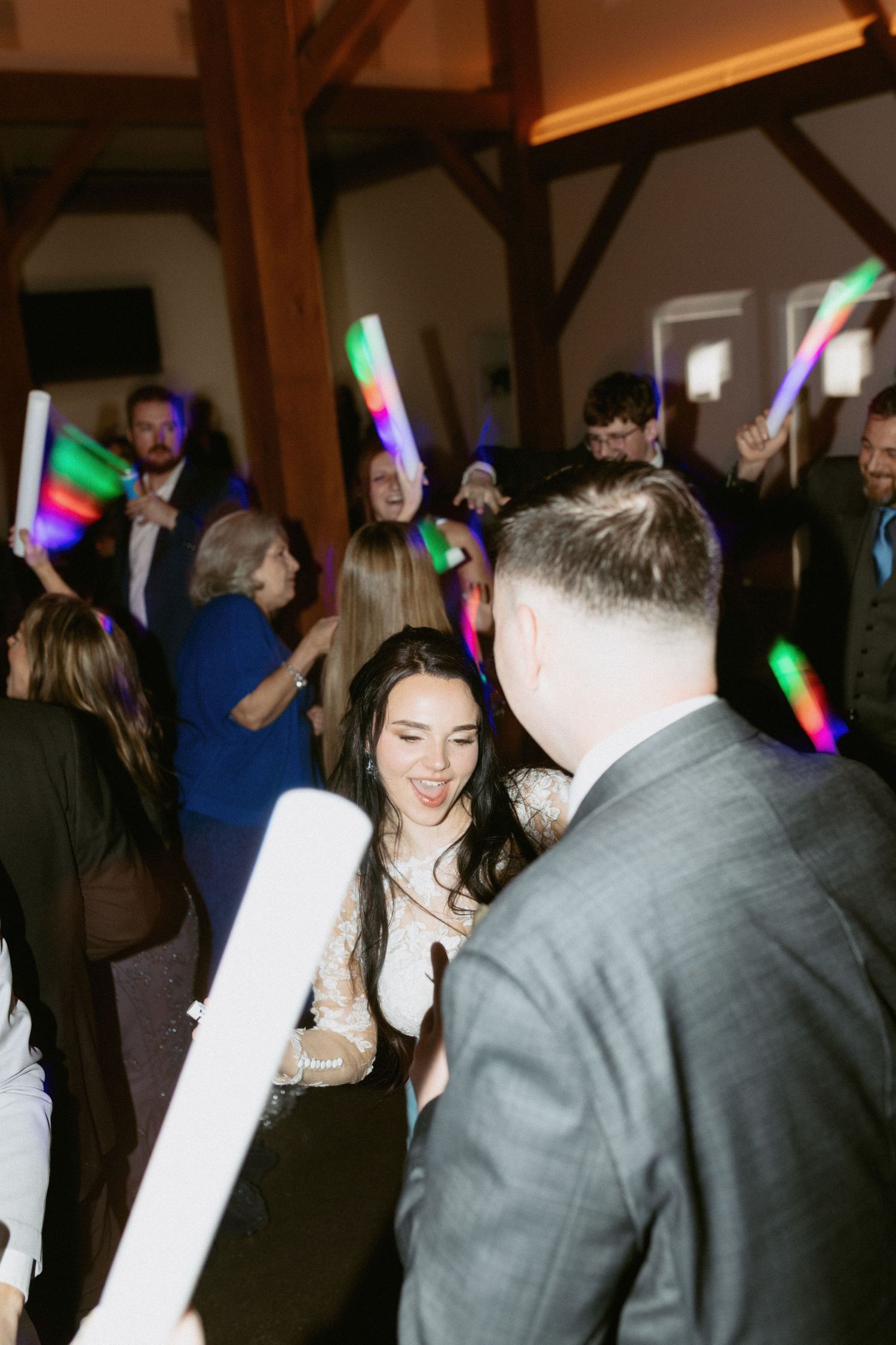 Guests dancing at a wedding reception with colorful disco lights illuminating the rustic wooden venue.