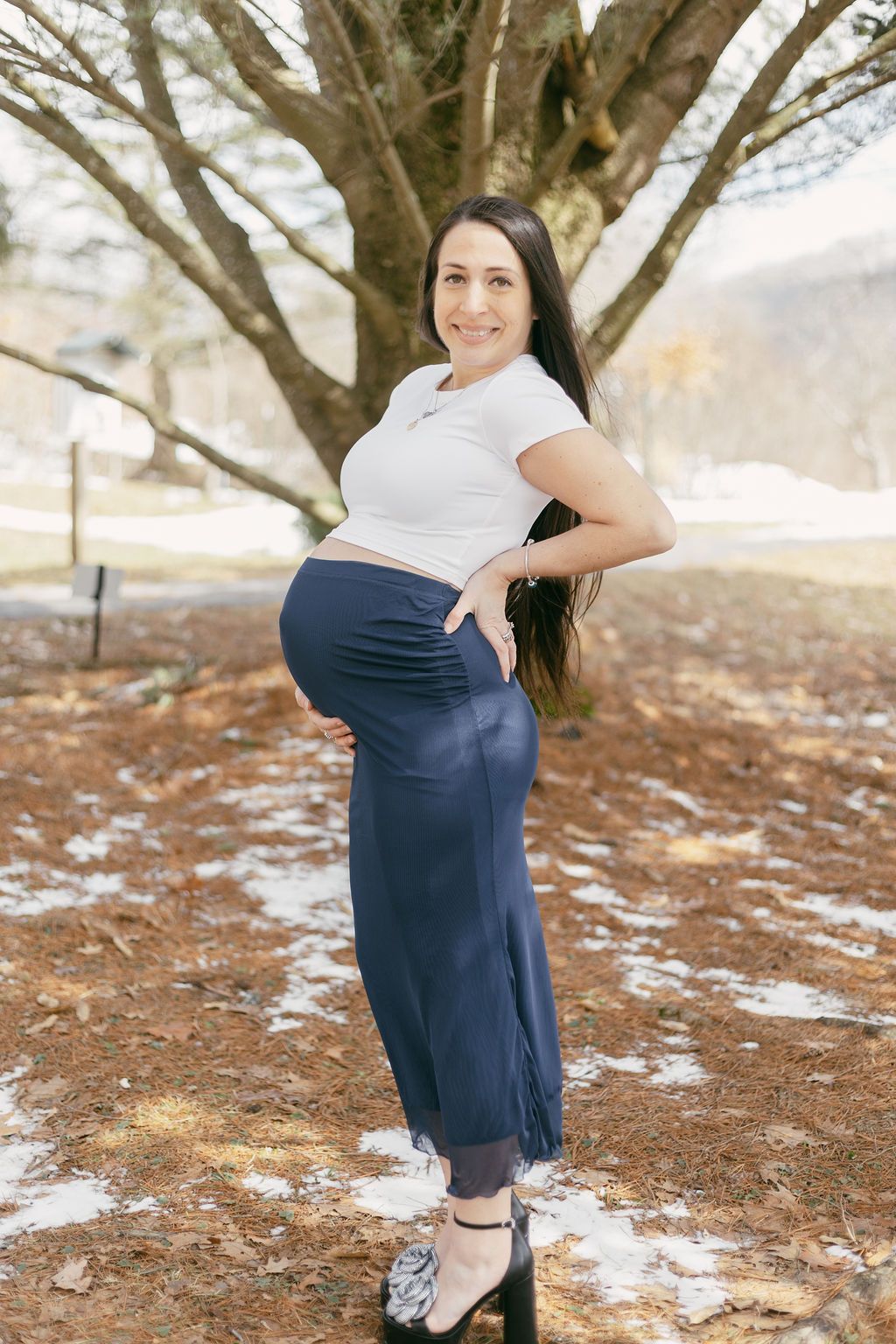 Maternity portrait of woman in white top and navy skirt posing outdoors.