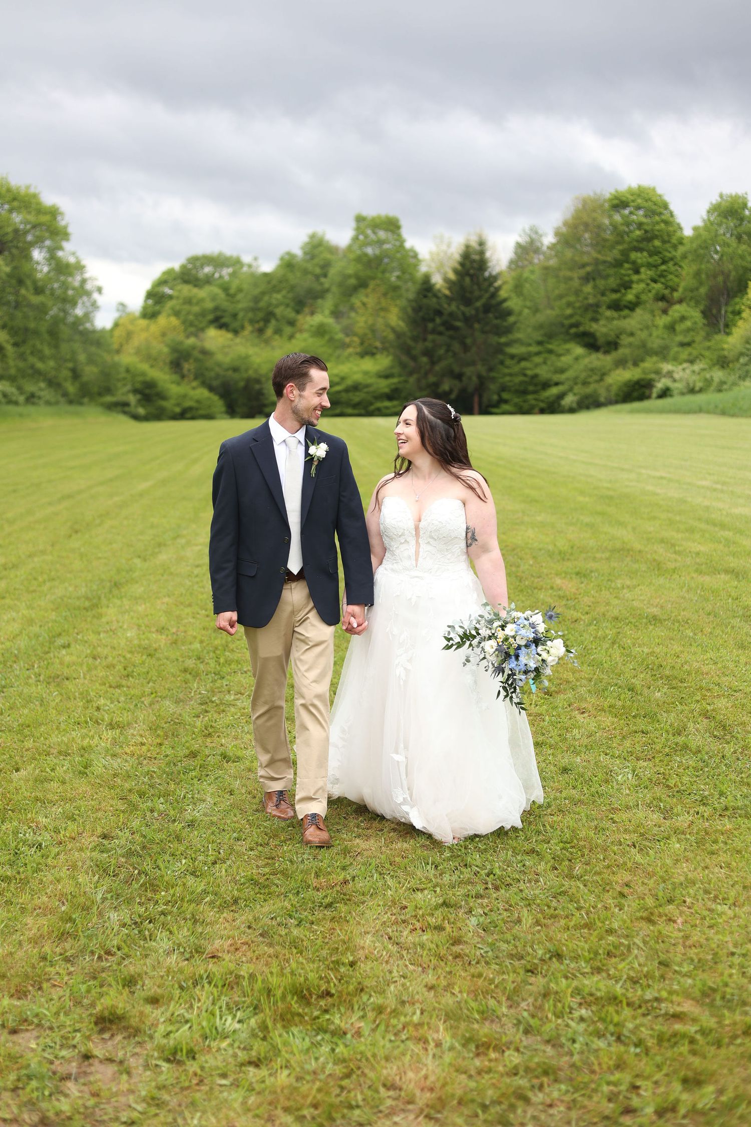 Couple walks hand in hand across a green hillside on their wedding day.