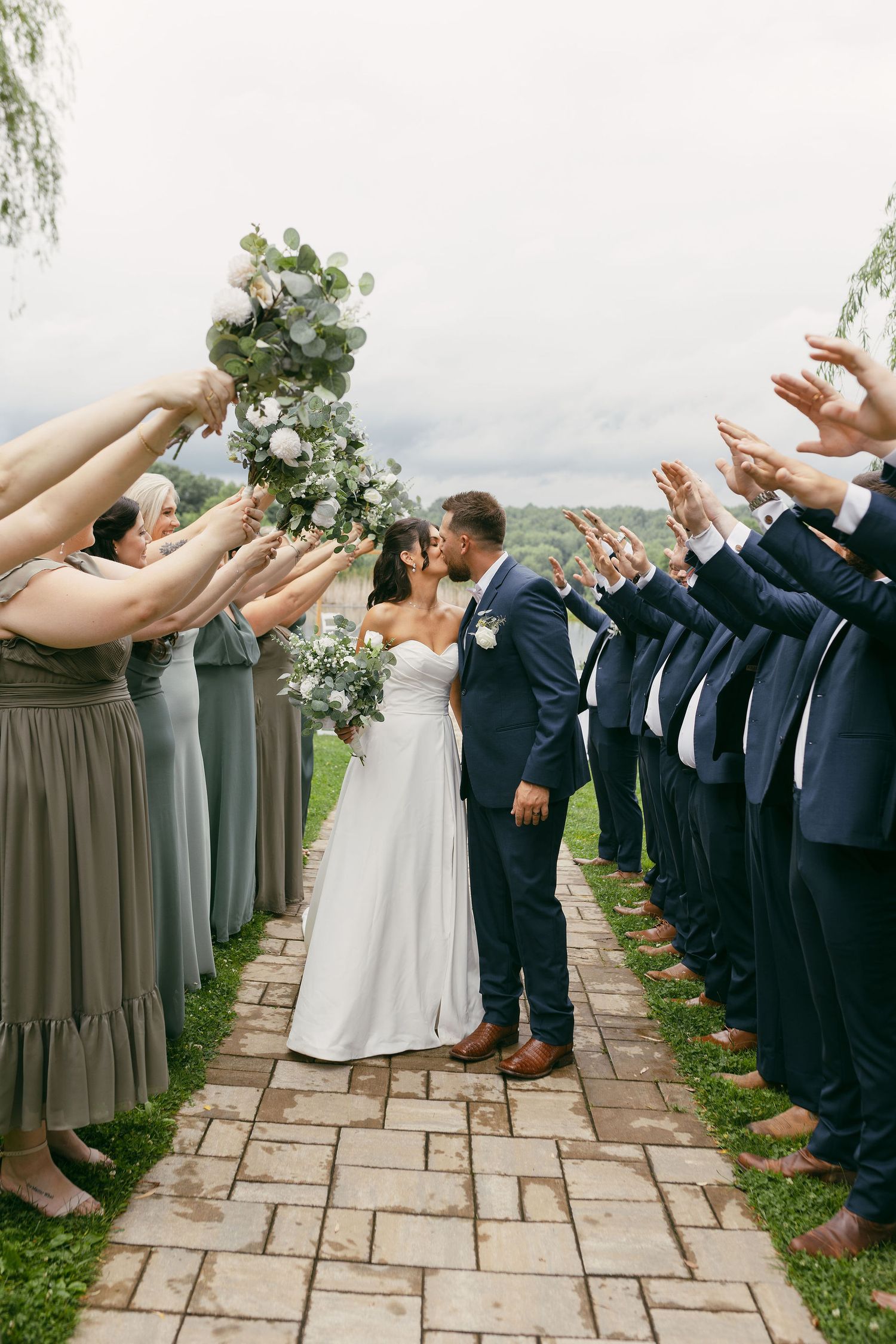 Wedding party forms a line on stone path with bridesmaids in grey and groomsmen in navy suits.