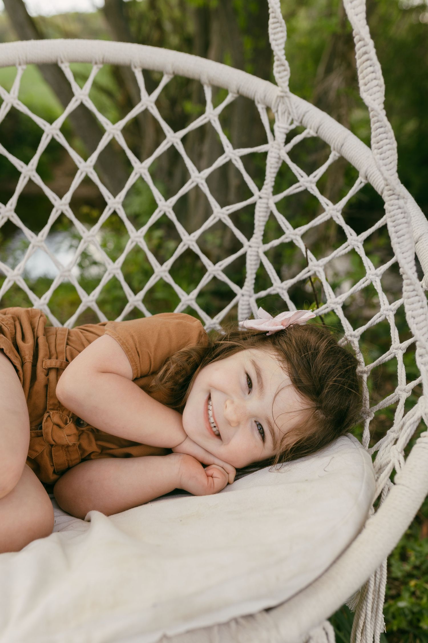 Child relaxing in a white macrame hammock swing outdoors.