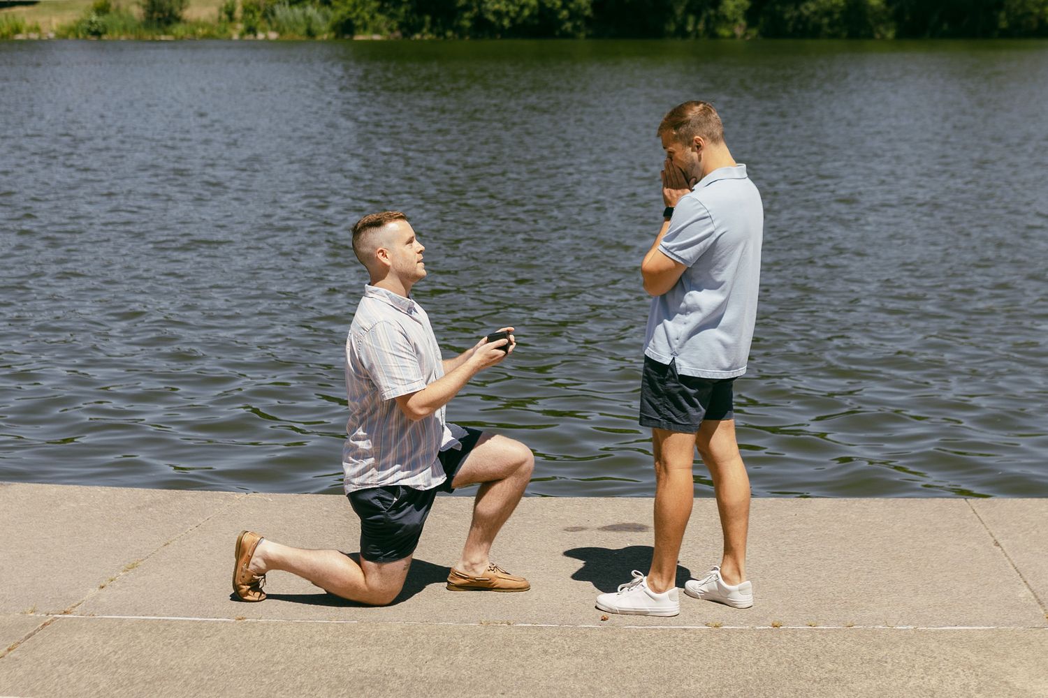 A proposal moment captured by the water as one person kneels with a ring.
