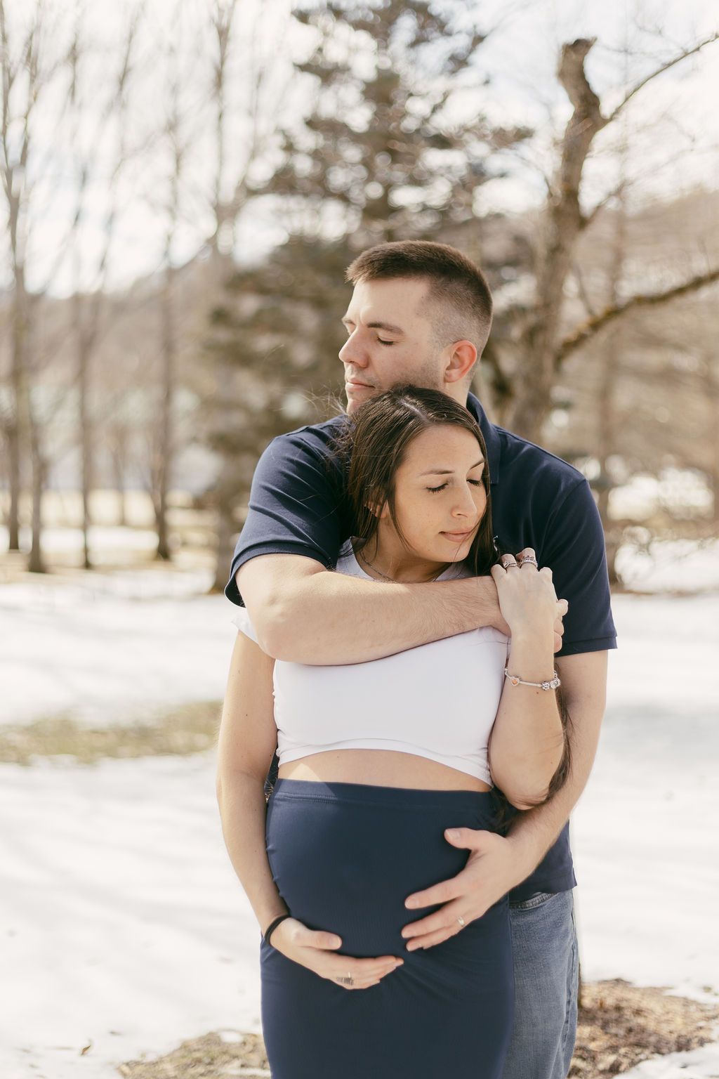 Couple sharing intimate moments in a winter landscape with bare trees in background.