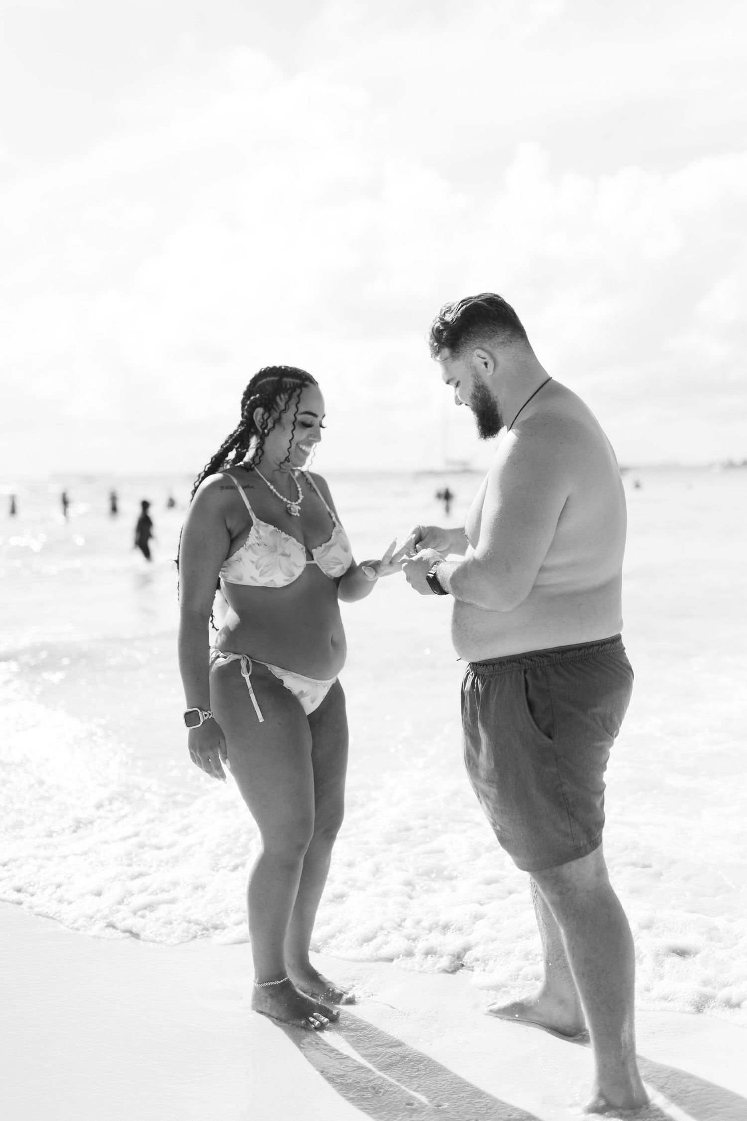 Black and white photo of a couple sharing a romantic moment on a beach, with ocean waves in the background.