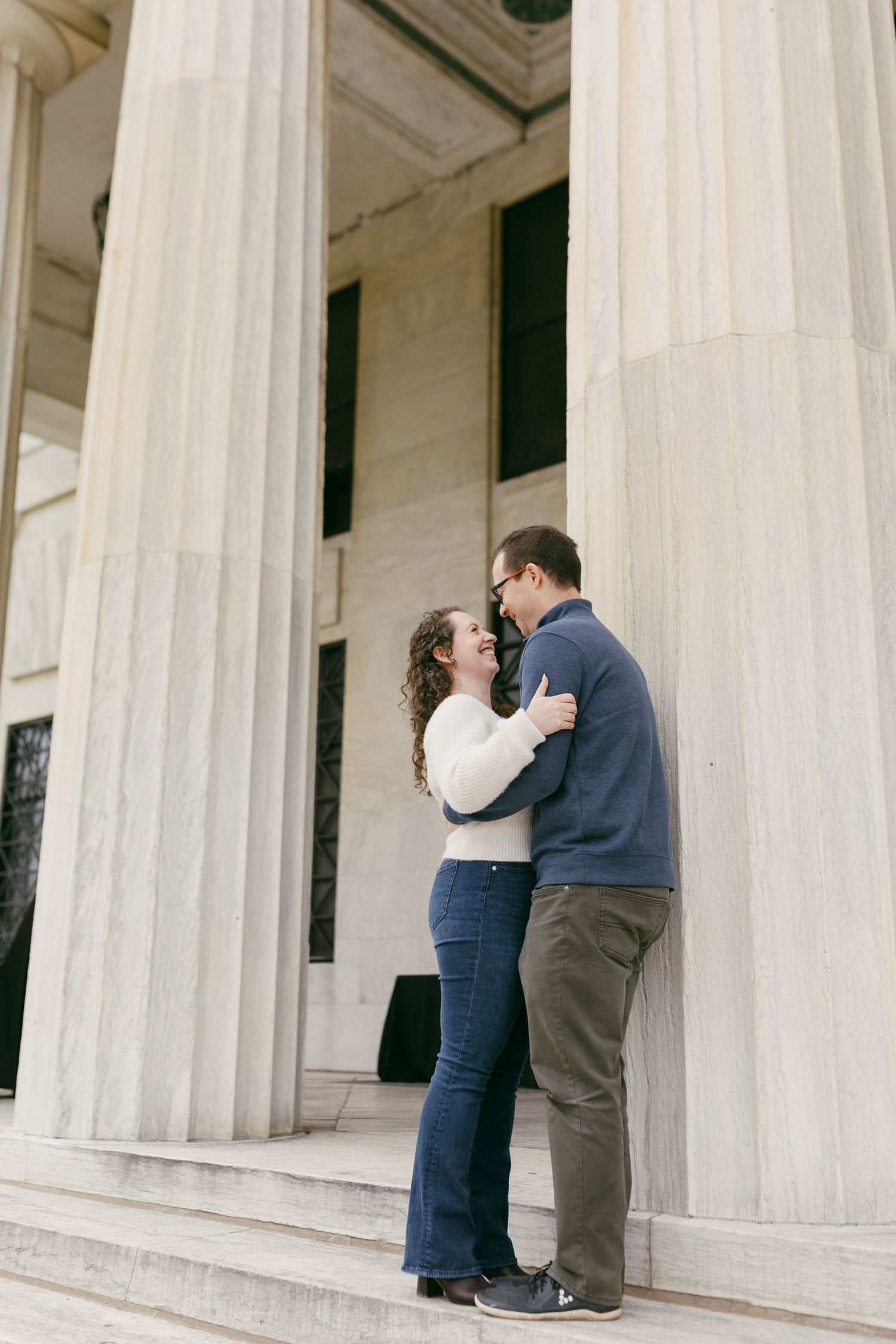 Couple embracing and smiling on steps of a neoclassical building with large stone columns.