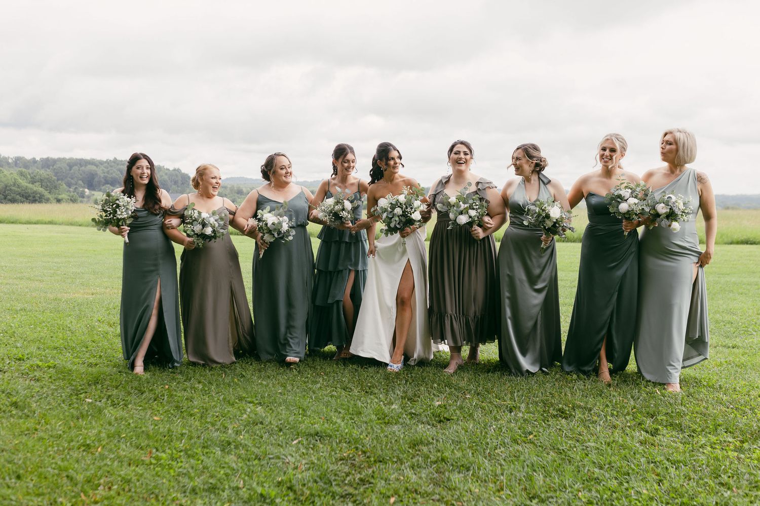 Wedding party members sit in a row on grass wearing coordinated formal attire.